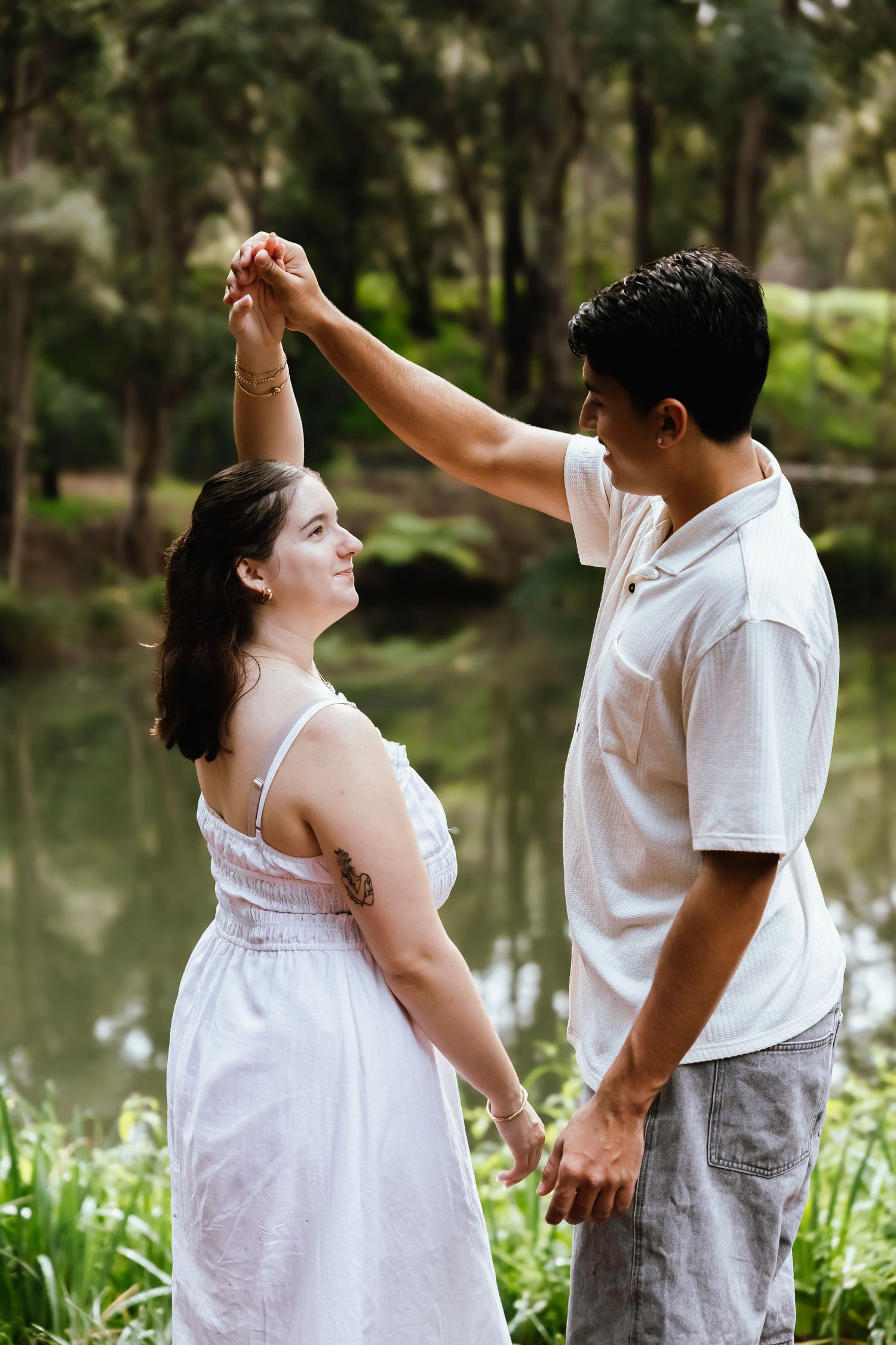 Couple dancing and holding hands near a serene pond in a lush green garden.