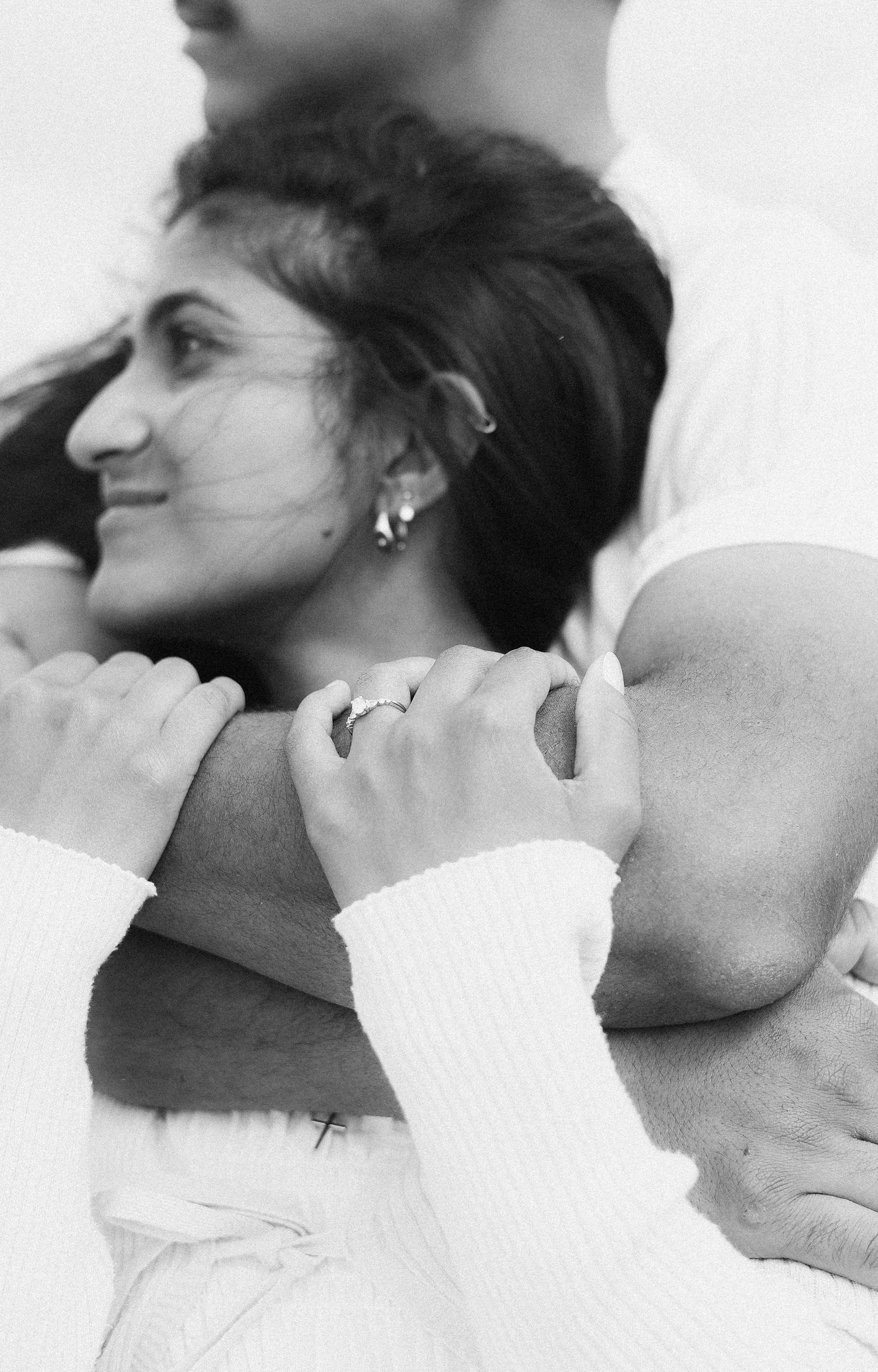 Black and white close-up of woman hugging mans arm showing engagement ring detail.