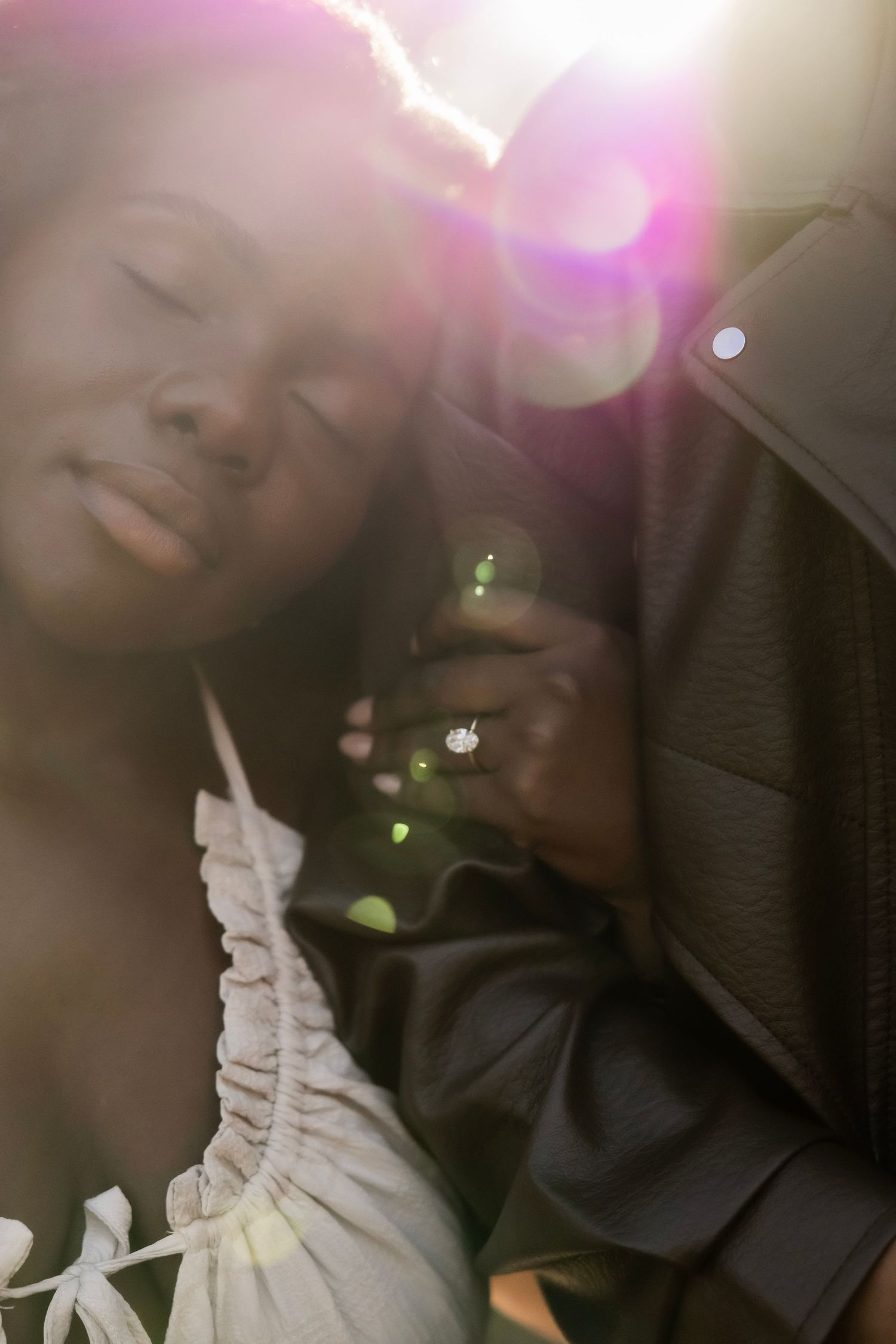 Close-up of a woman showing off her engagement ring with beautiful sun flare bokeh in the background.