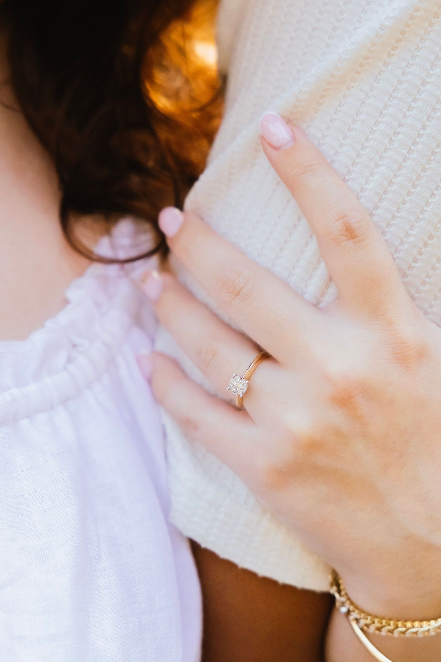 Close-up of a gold solitaire diamond engagement ring on a woman's hand resting on a sweater.