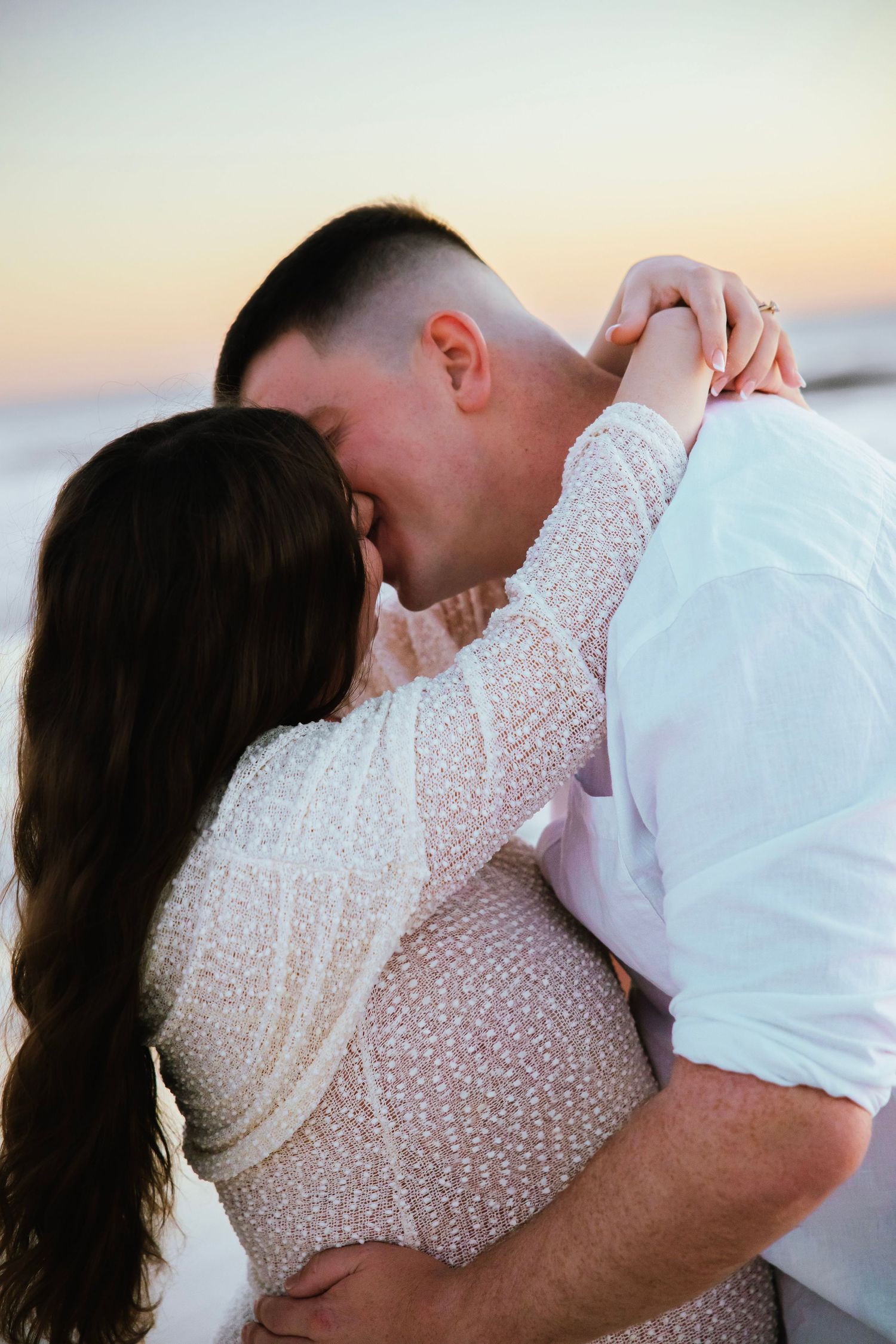 Expecting couple embracing and kissing at beach during colorful pastel sunset, maternity photo.