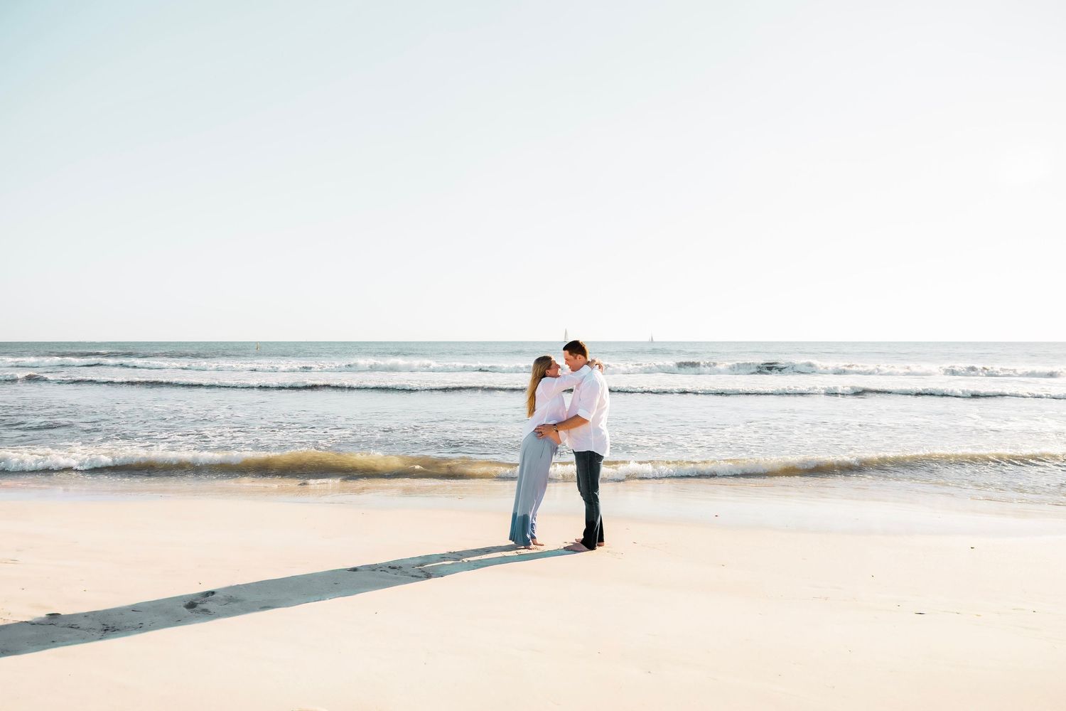 Couple embracing romantically on a sunny beach with ocean waves in the background.