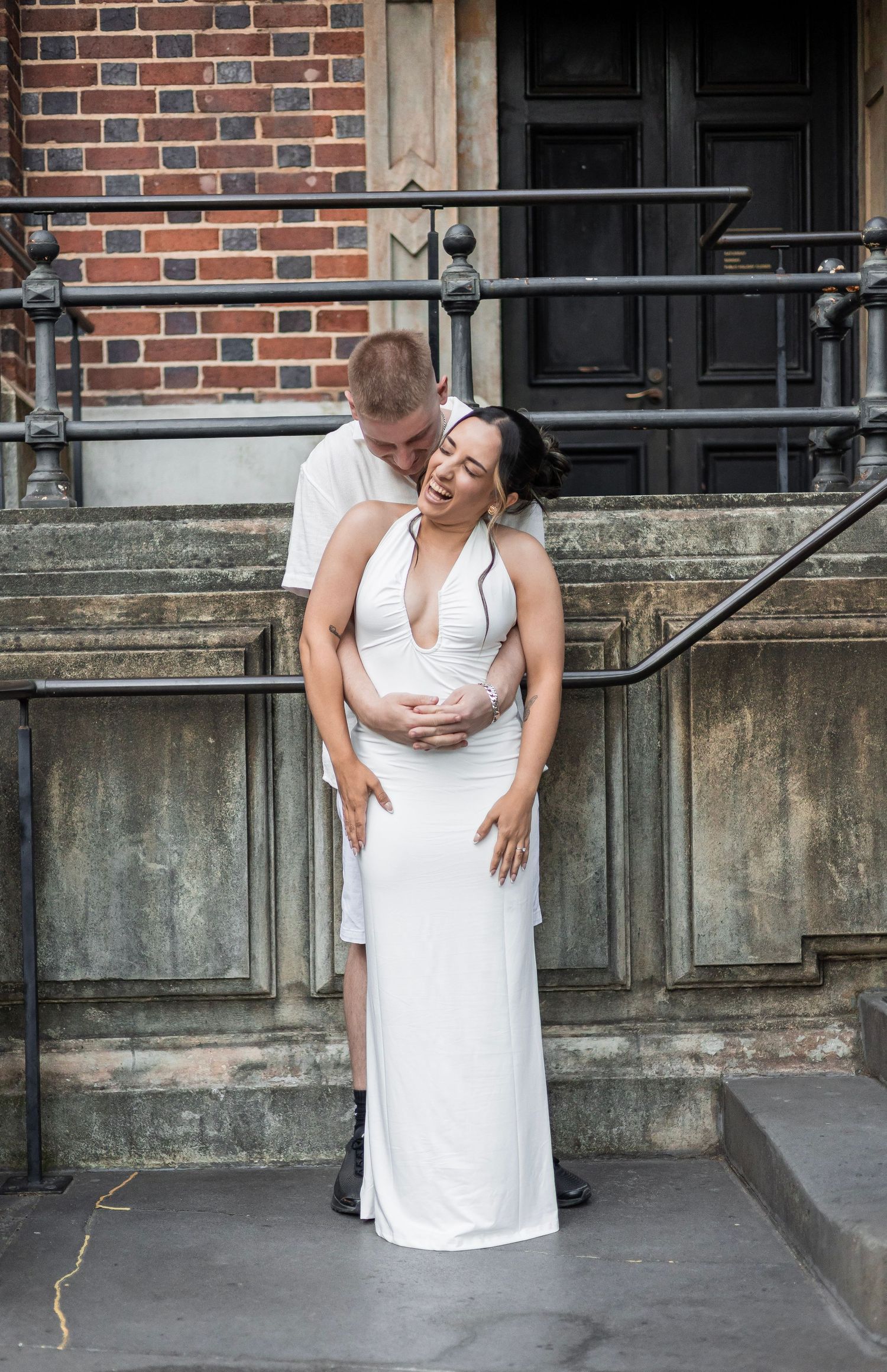 Couple sharing tender moment on stone steps, man kissing pregnant womans head as she cradles belly.