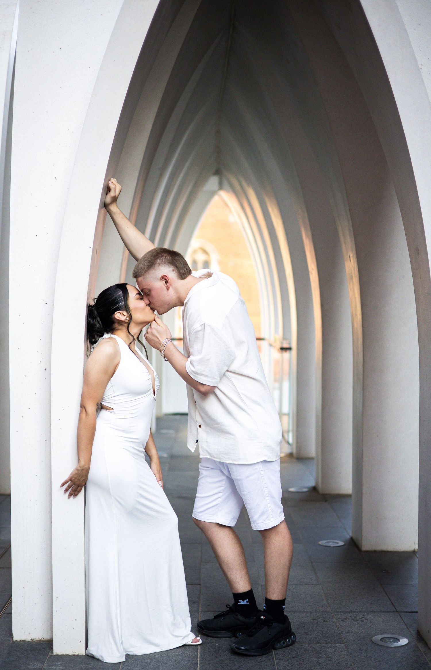Couple in white sharing a romantic kiss under elegant arched colonnade.