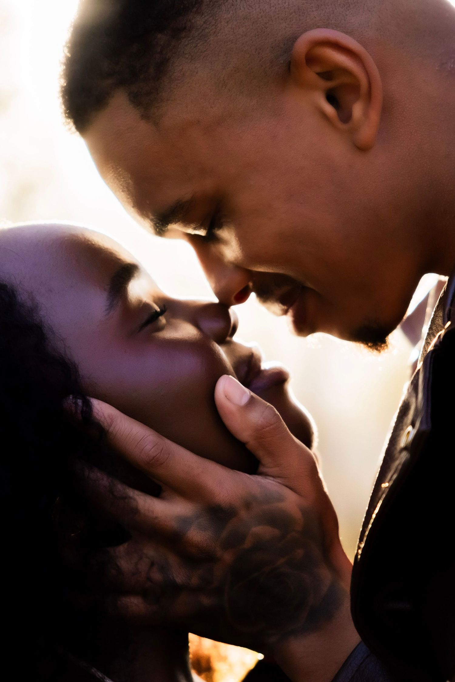 A tattooed couple shares a romantic moment, faces close together, bathed in warm golden backlight.
