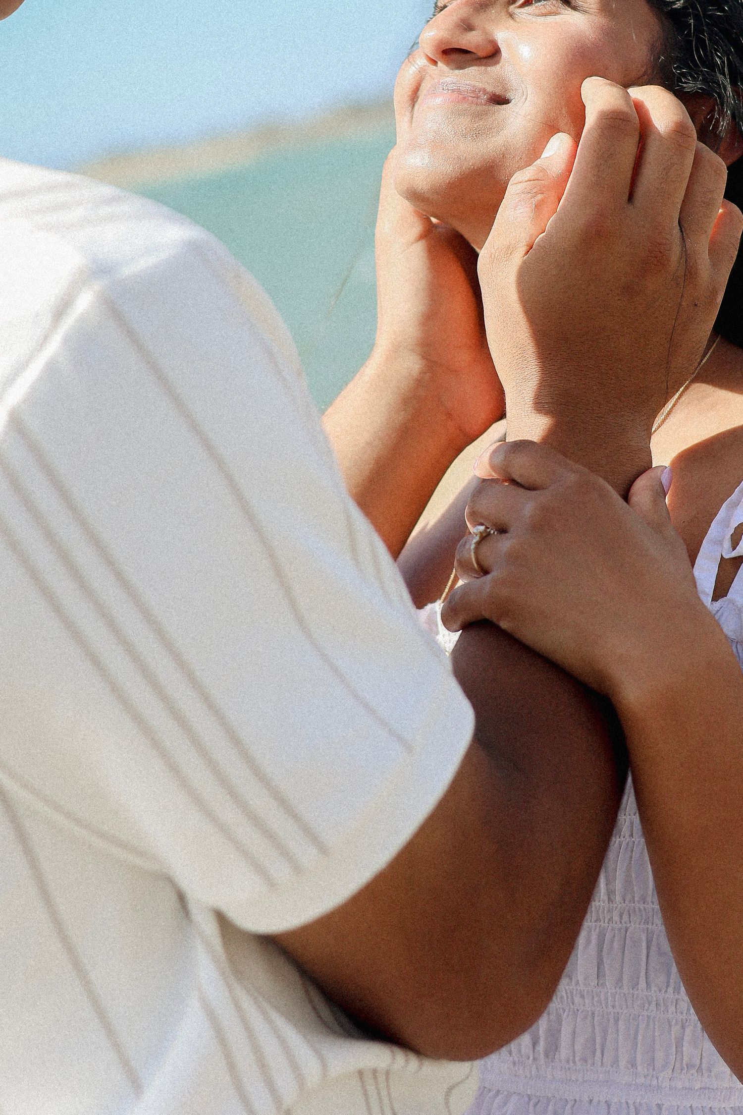Close-up of a man tenderly holding a smiling woman's face, with an engagement ring visible.