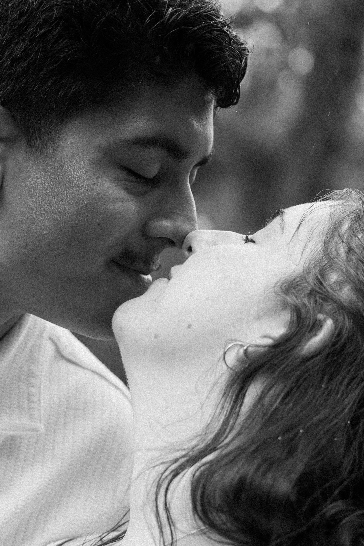 Black and white photo of a romantic couple about to kiss, with soft bokeh background.