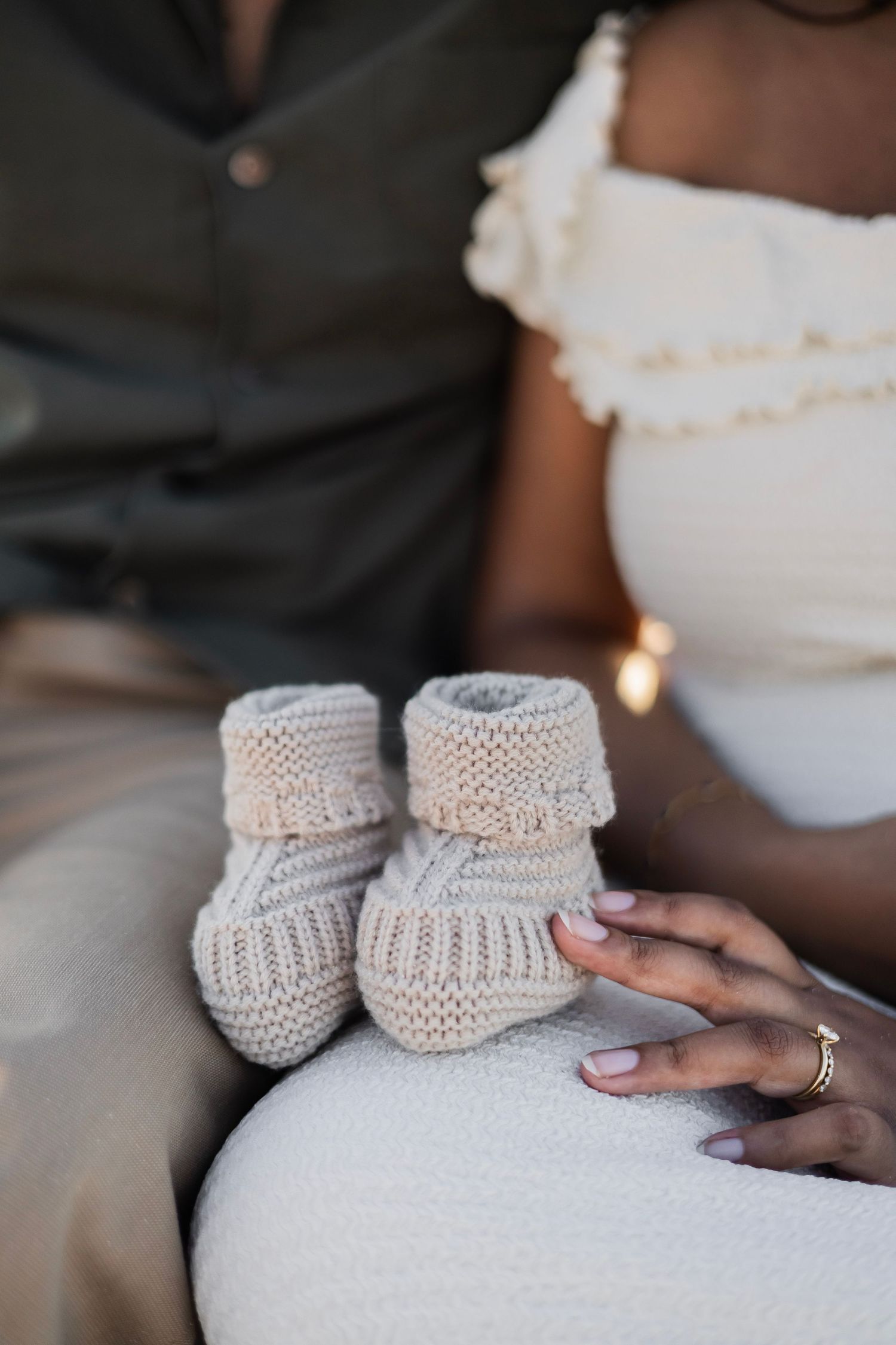 Tiny knit baby booties resting on a pregnant woman's belly, held gently by her hand with a ring.