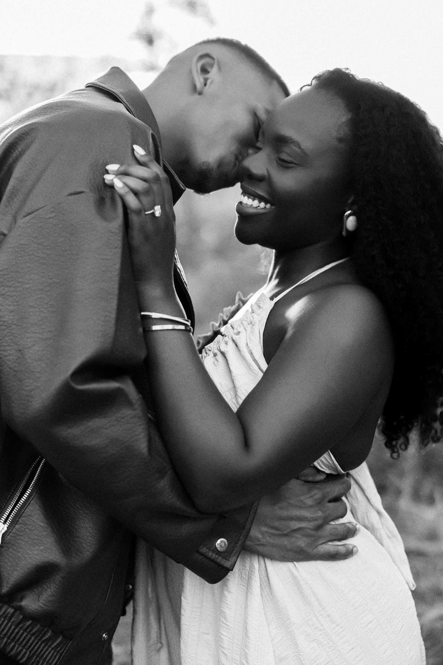 Black and white photo of a joyful couple embracing and sharing a romantic moment outdoors.
