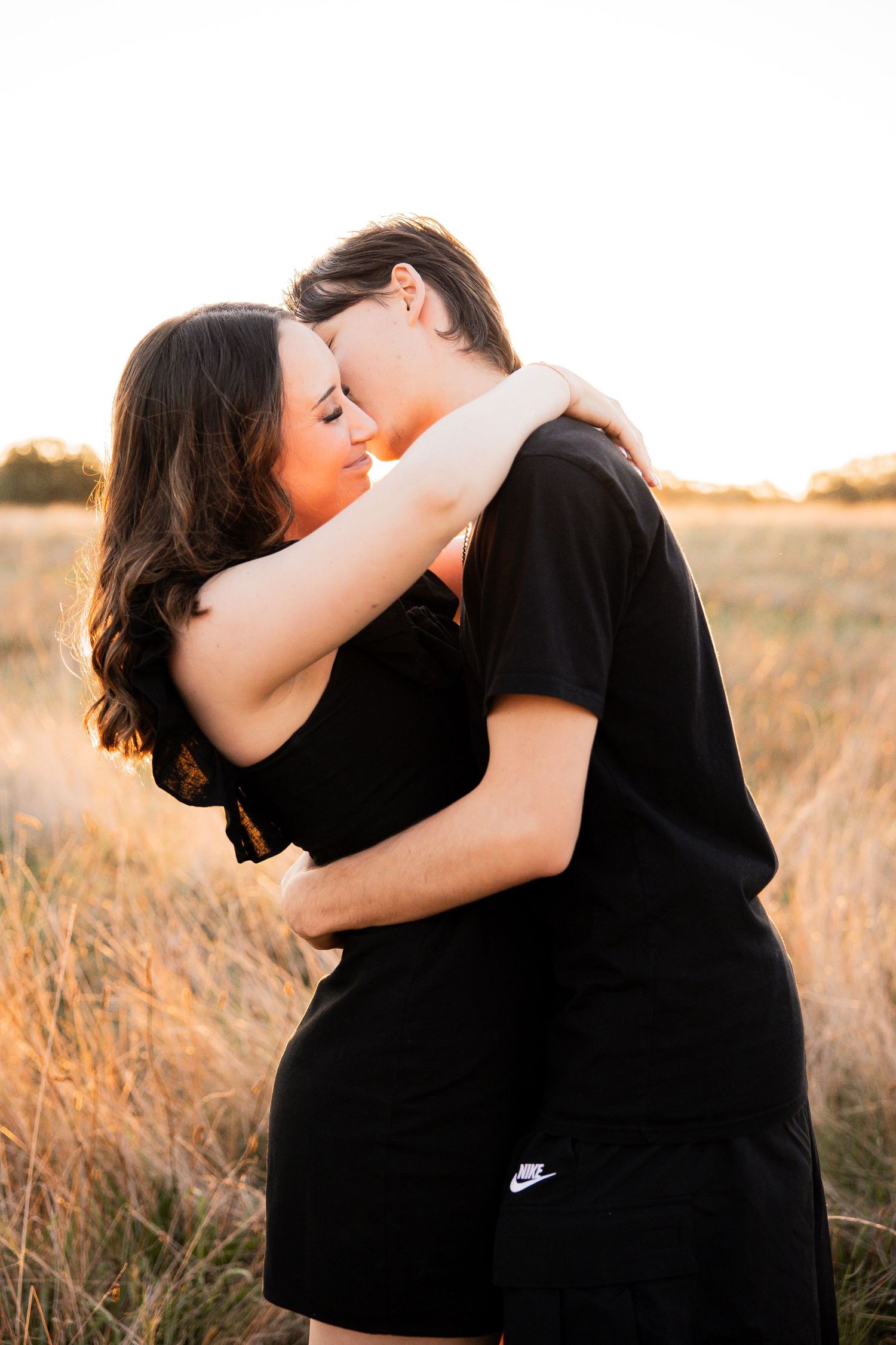 Couple embracing and kissing in golden field at sunset wearing matching black outfits.