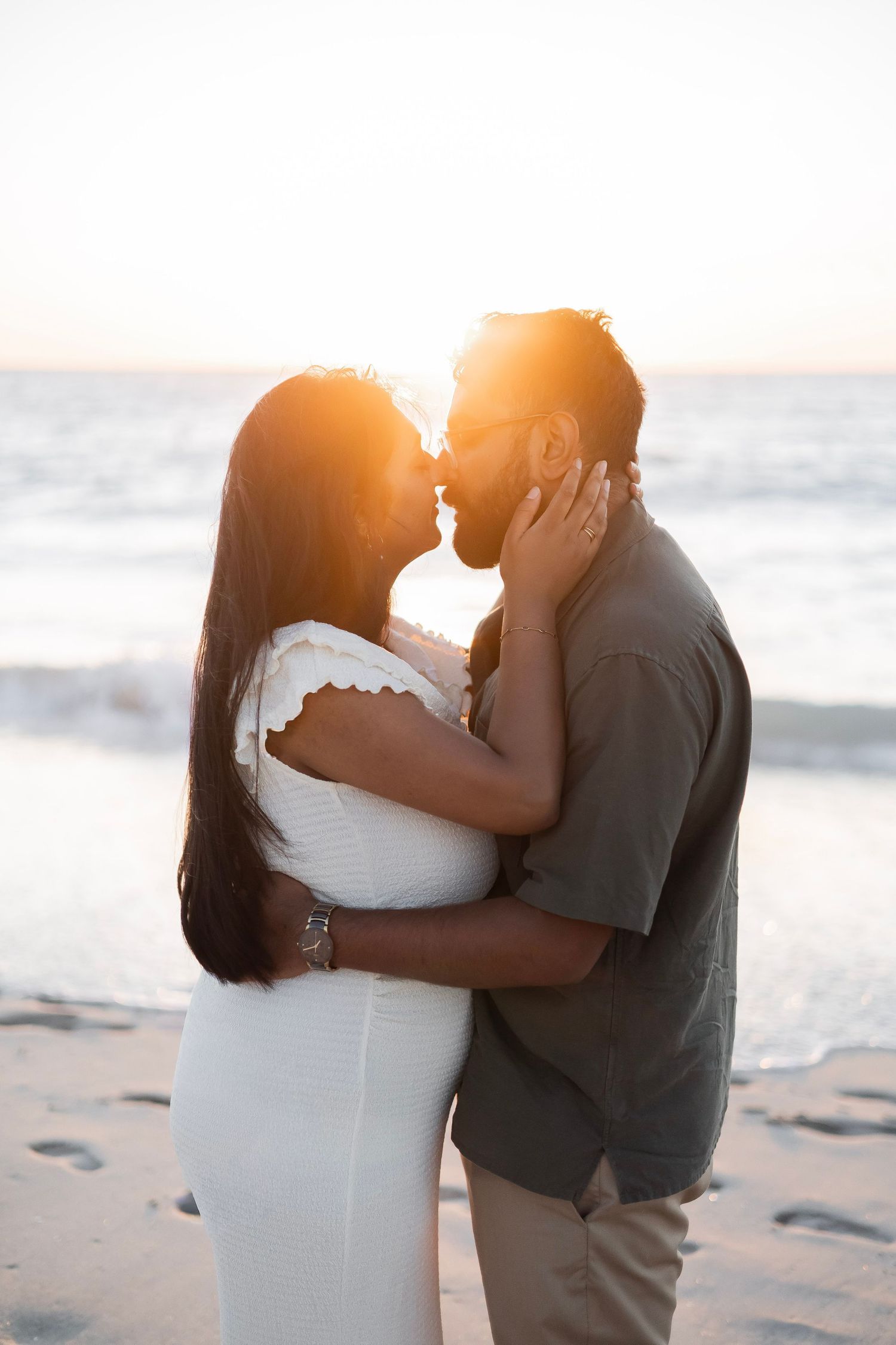 Couple sharing a tender sunset kiss on the beach, silhouetted by warm golden backlight.
