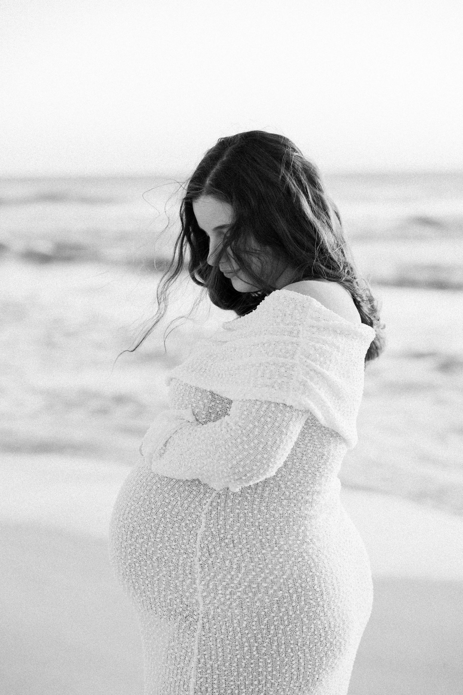 Elegant black and white maternity portrait of pregnant woman in lace dress on windy beach.