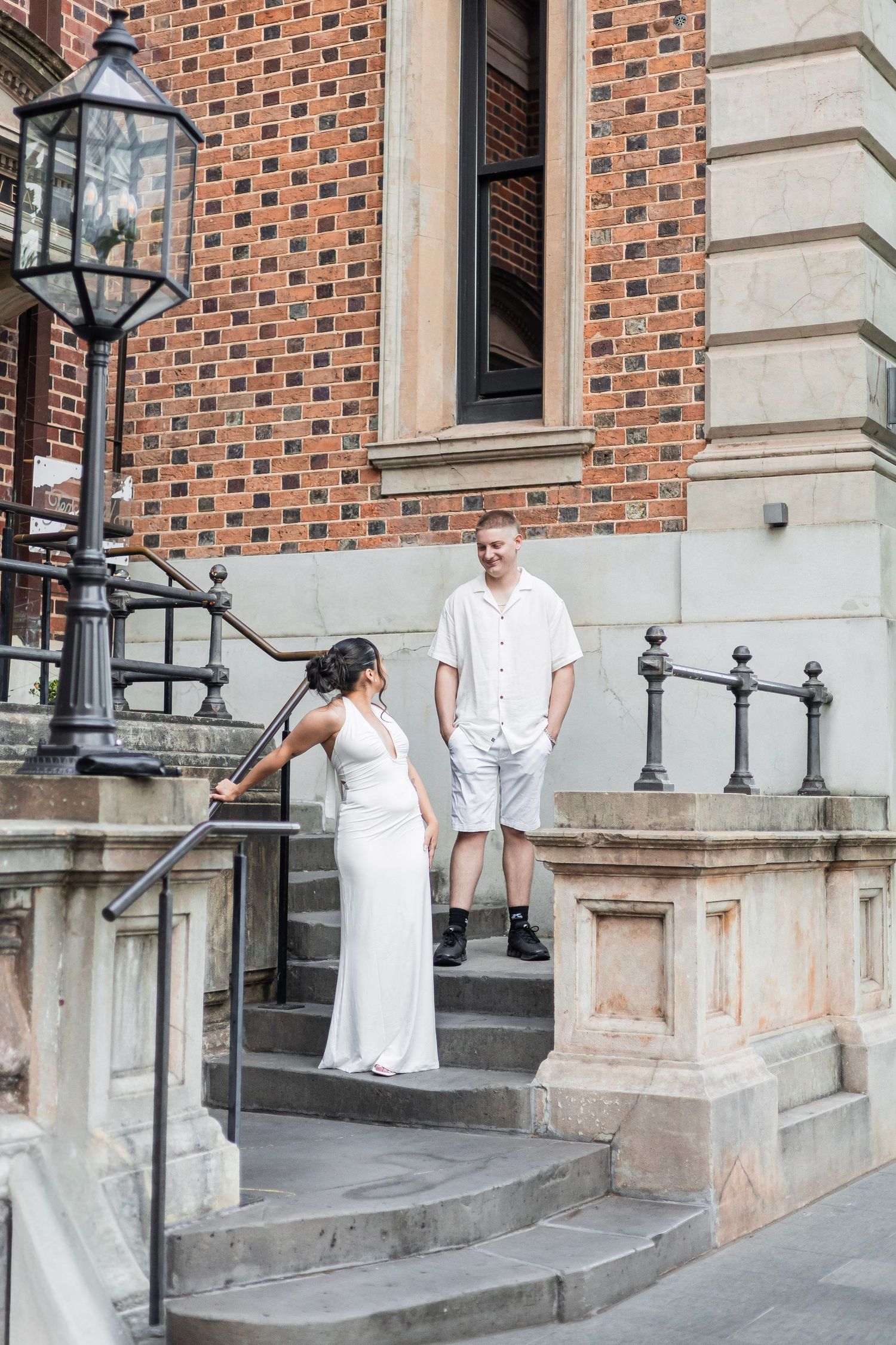 Bride and groom in white outfits sharing a moment on historic building steps.