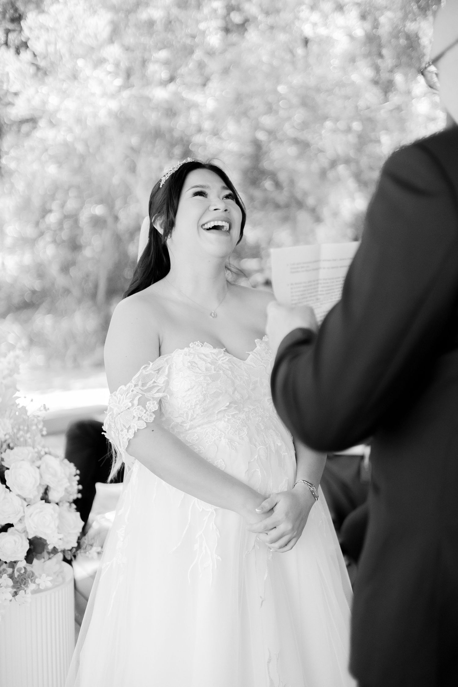 Black and white photo of radiant bride laughing joyfully during outdoor wedding ceremony.