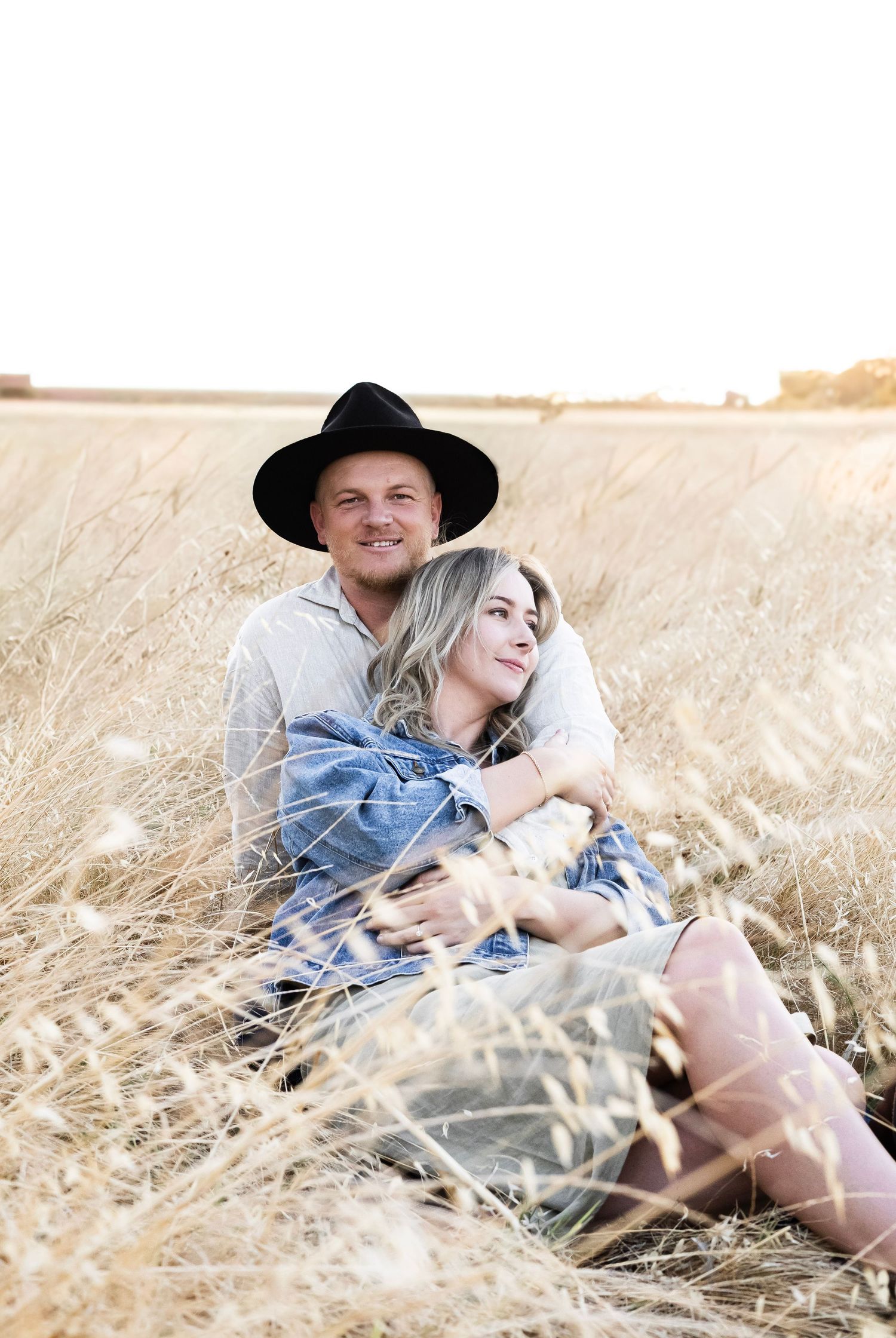 Couple embracing and smiling while sitting together in a golden dry grass field.