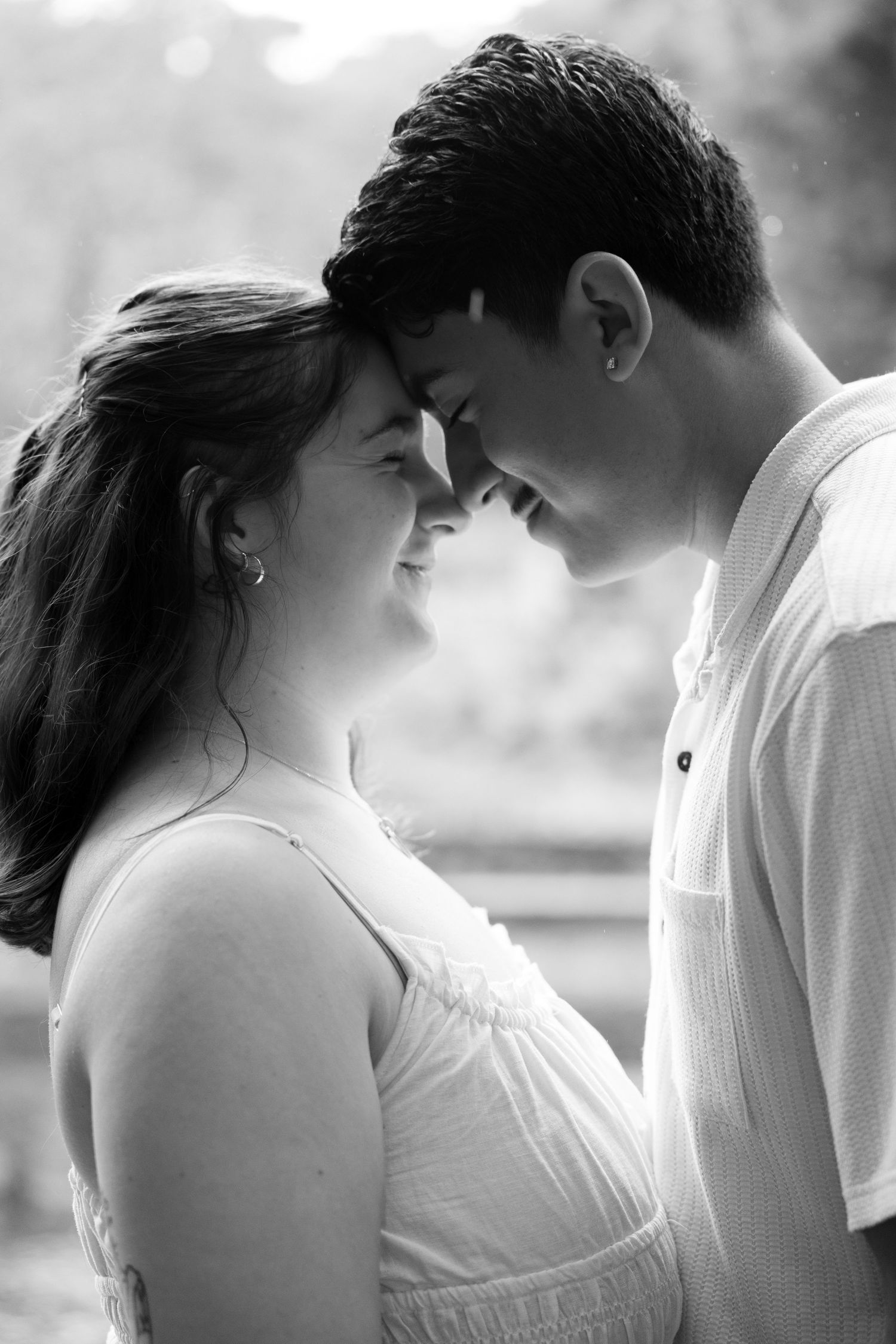 Black and white photo of a romantic couple touching foreheads, sharing an intimate moment outdoors.