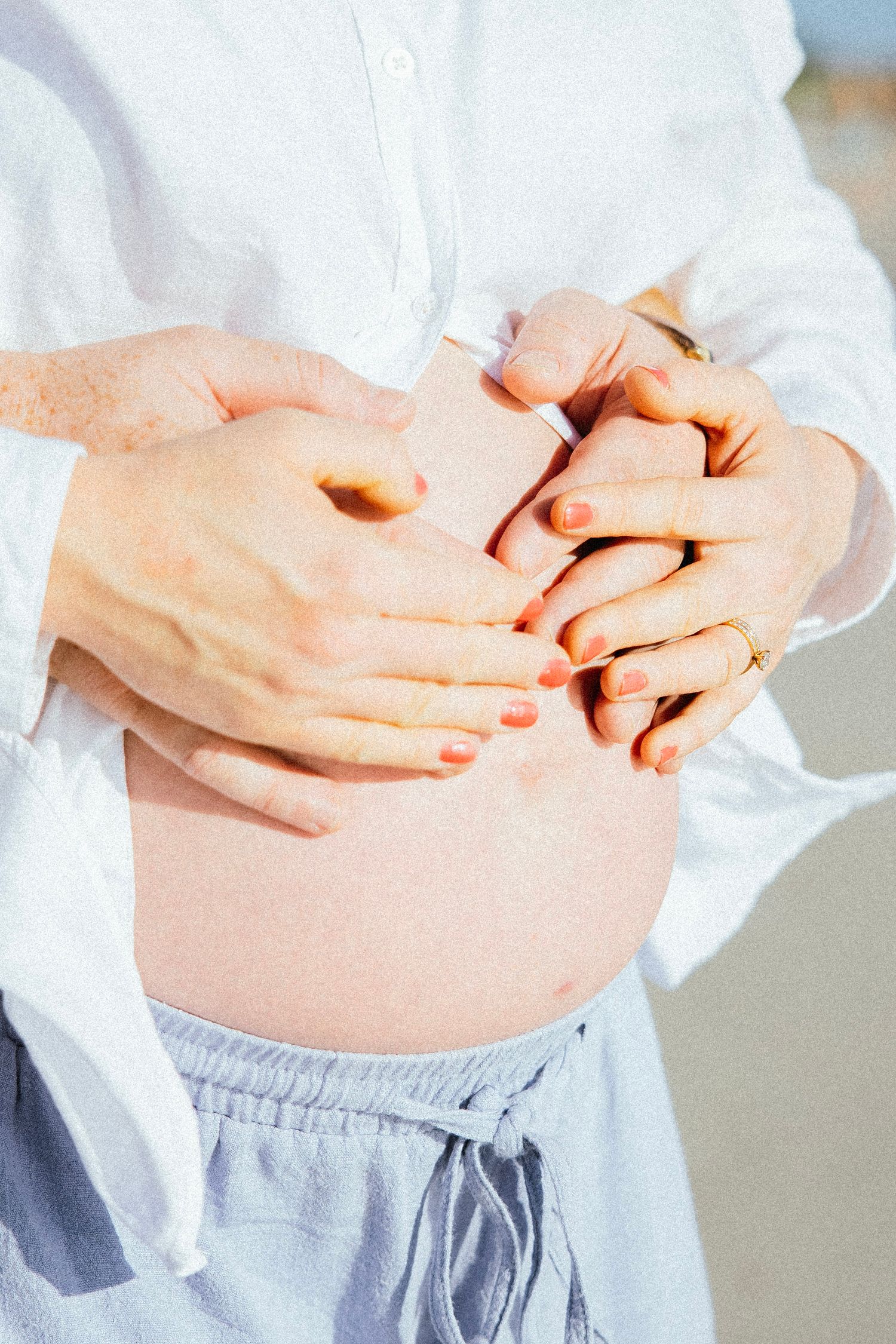 Close-up of pregnant belly with couple's hands forming heart shape, white shirts, maternity photo session.