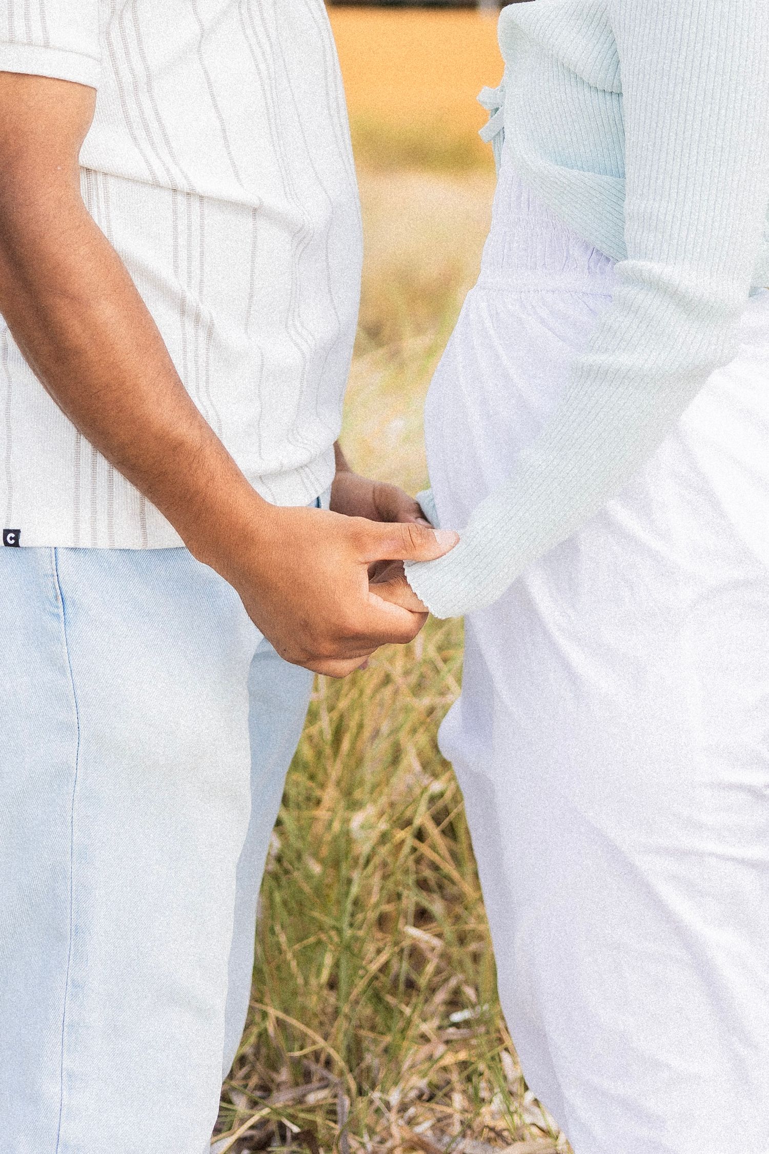 Close-up of interracial couple holding hands together in a grassy outdoor setting.