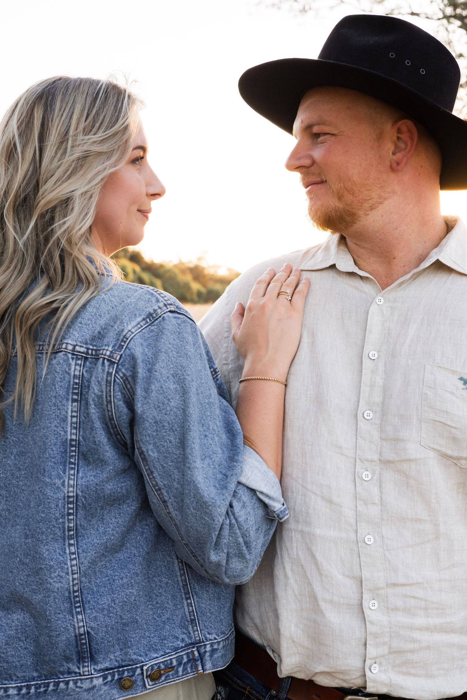 Couple gazing at each other at sunset, woman wearing denim jacket and man in cowboy hat.