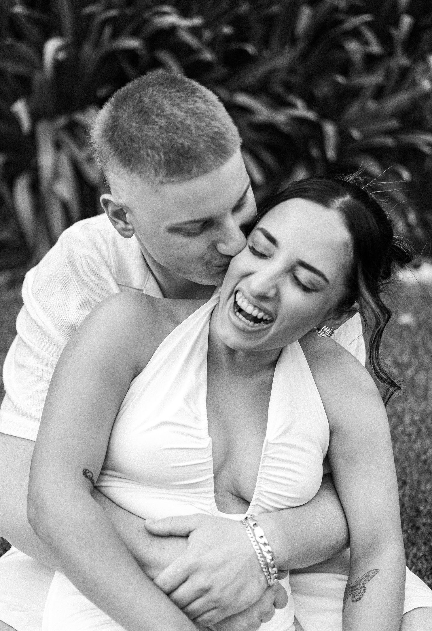 Black and white photo of laughing couple embracing in garden setting.