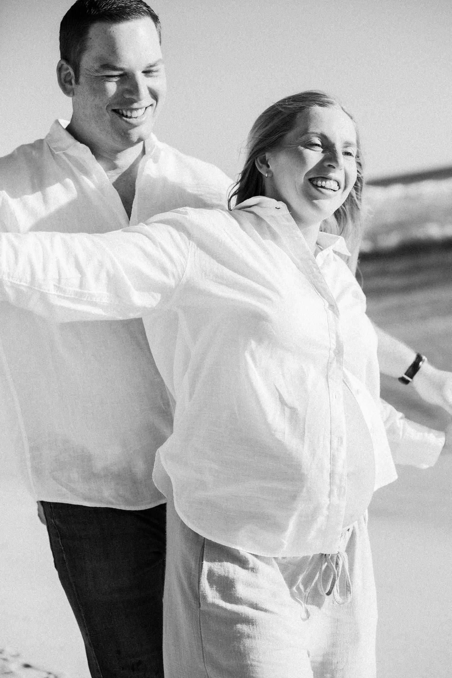 Happy couple in white shirts laughing together on sunny beach.