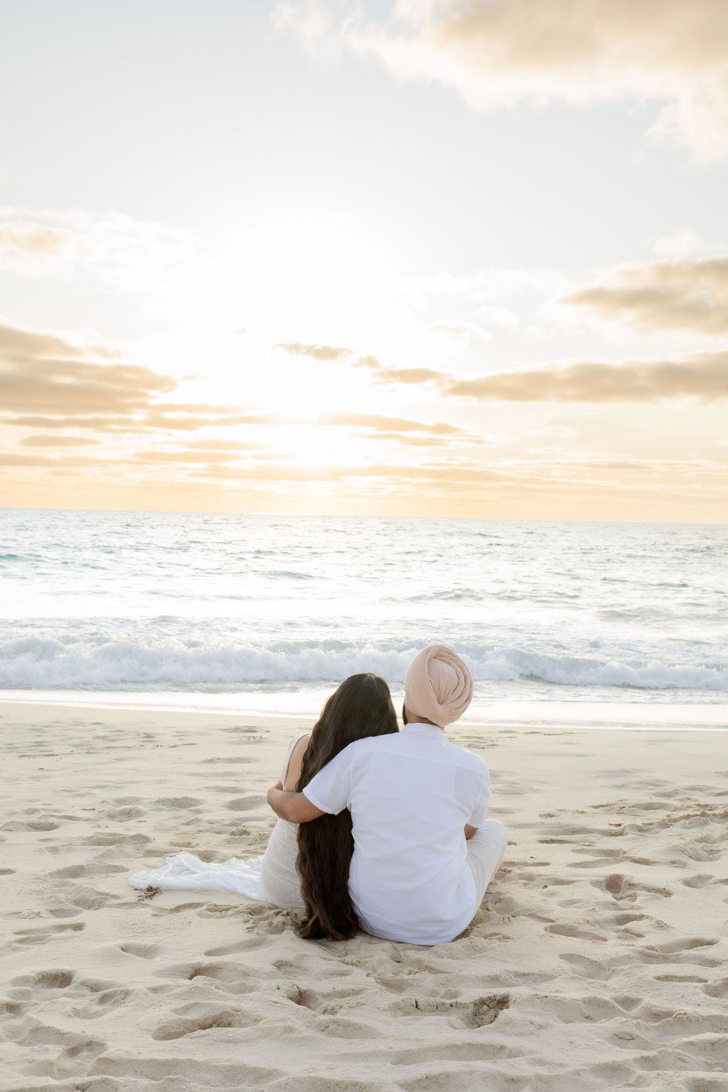 Couple sitting together on beach sand watching a beautiful ocean sunset.