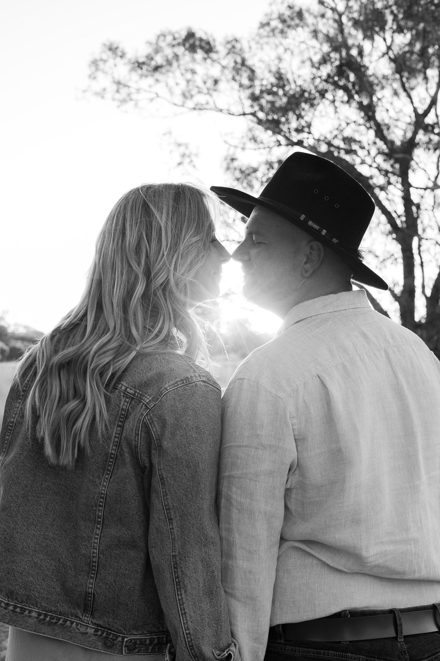 Black and white photo of couple sharing an intimate moment backlit by sunlight outdoors.