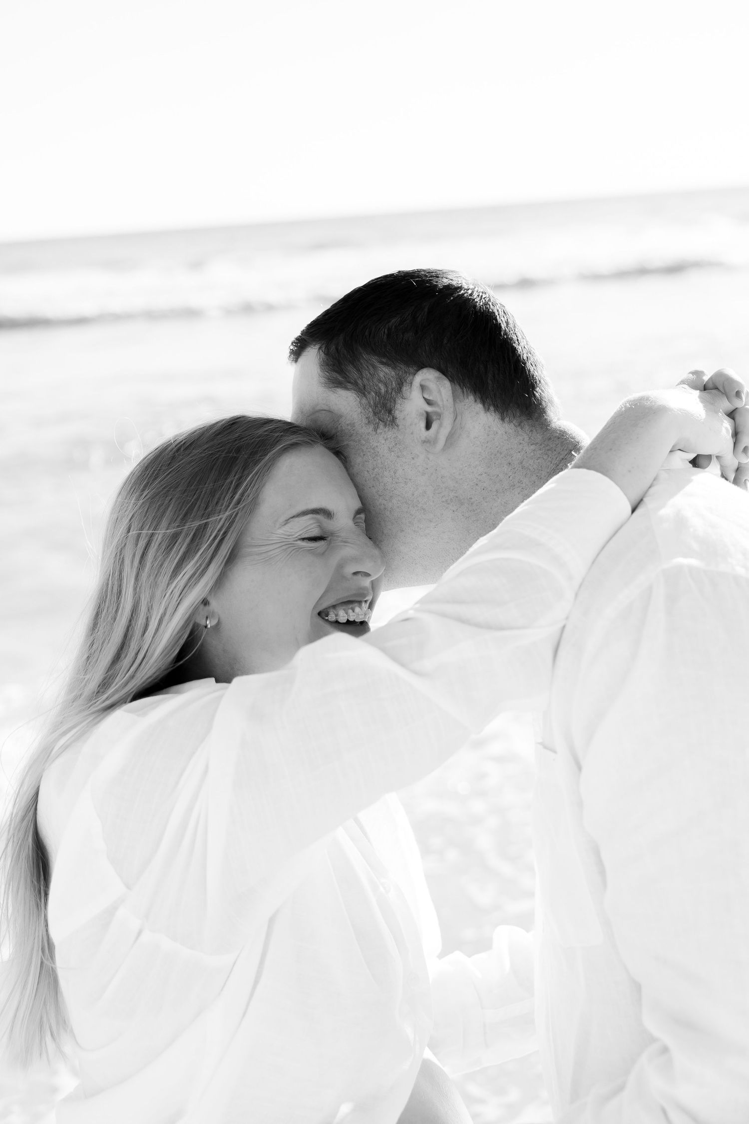 Black and white photo of a laughing couple sharing a romantic moment on the beach.