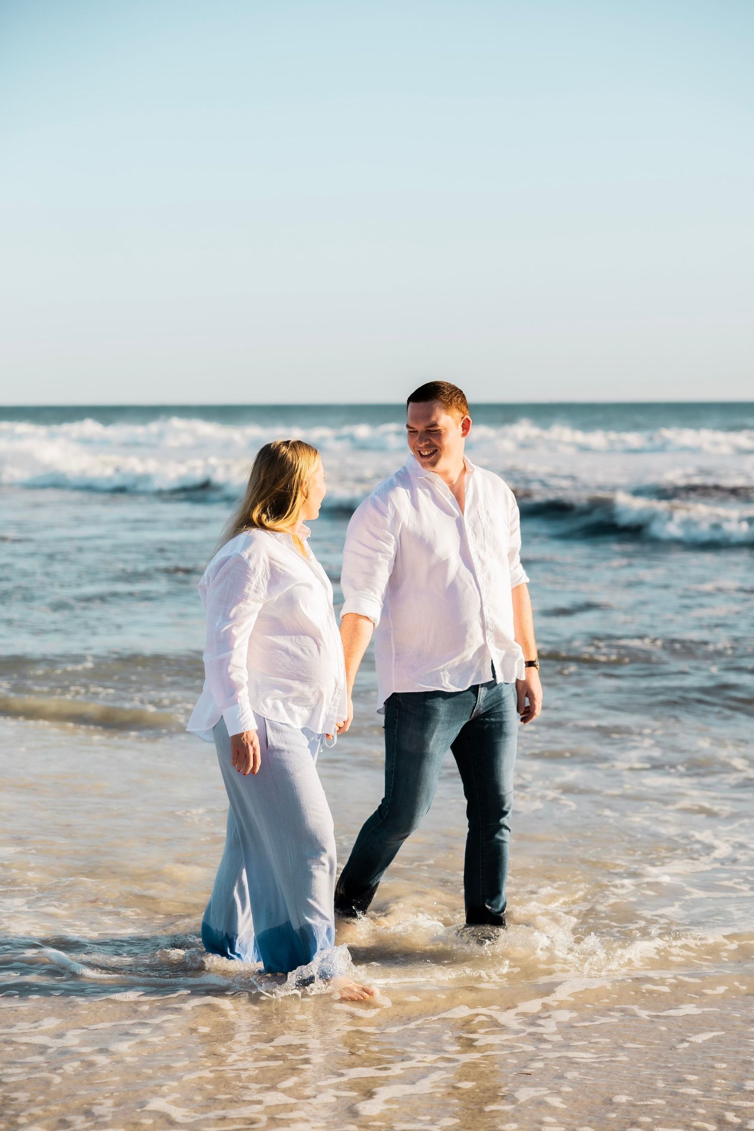 Couple walking and laughing together along the ocean shoreline on a sunny beach.