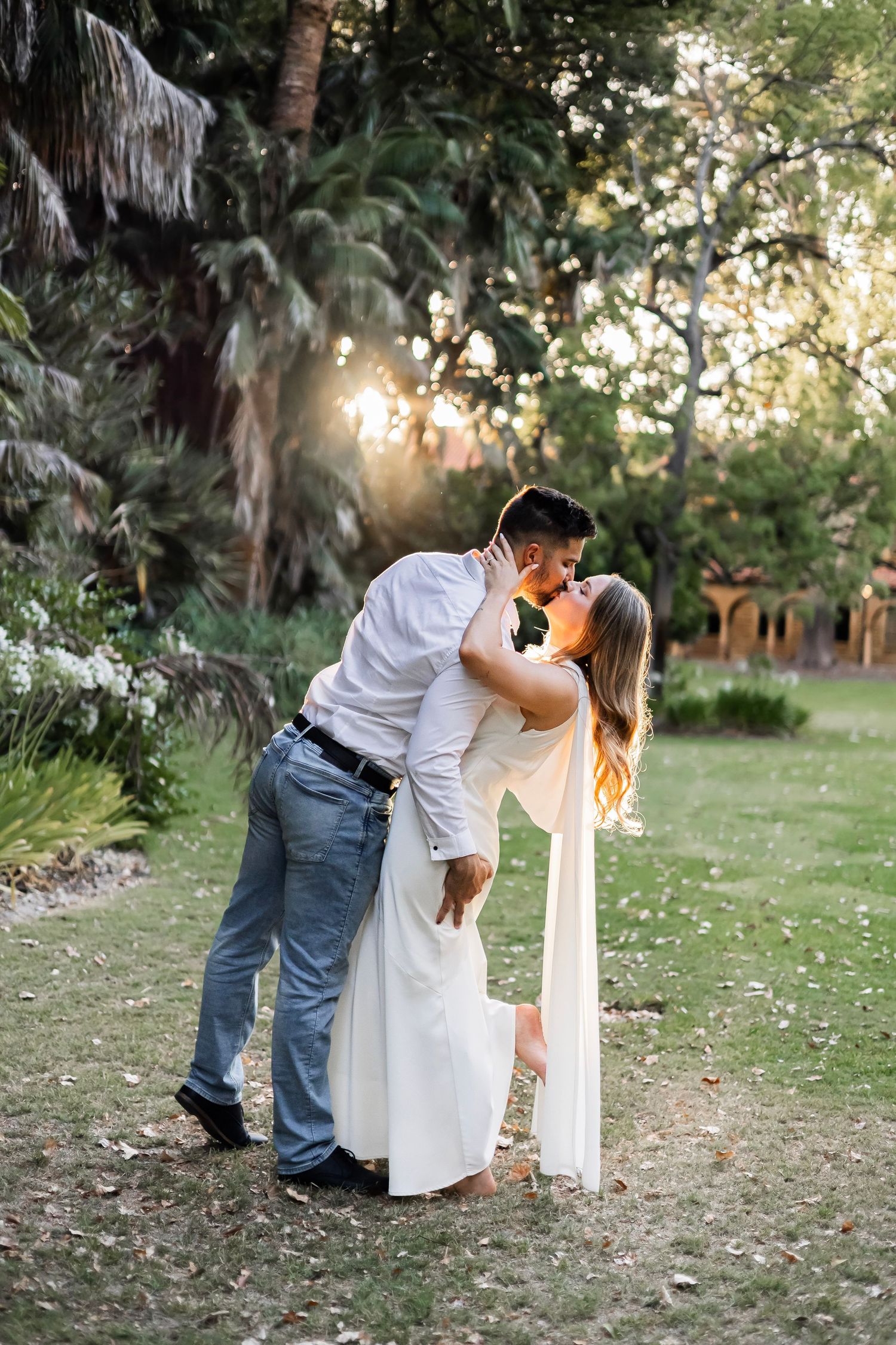 Couple sharing a passionate dip kiss in a sunlit garden with tropical palm trees.