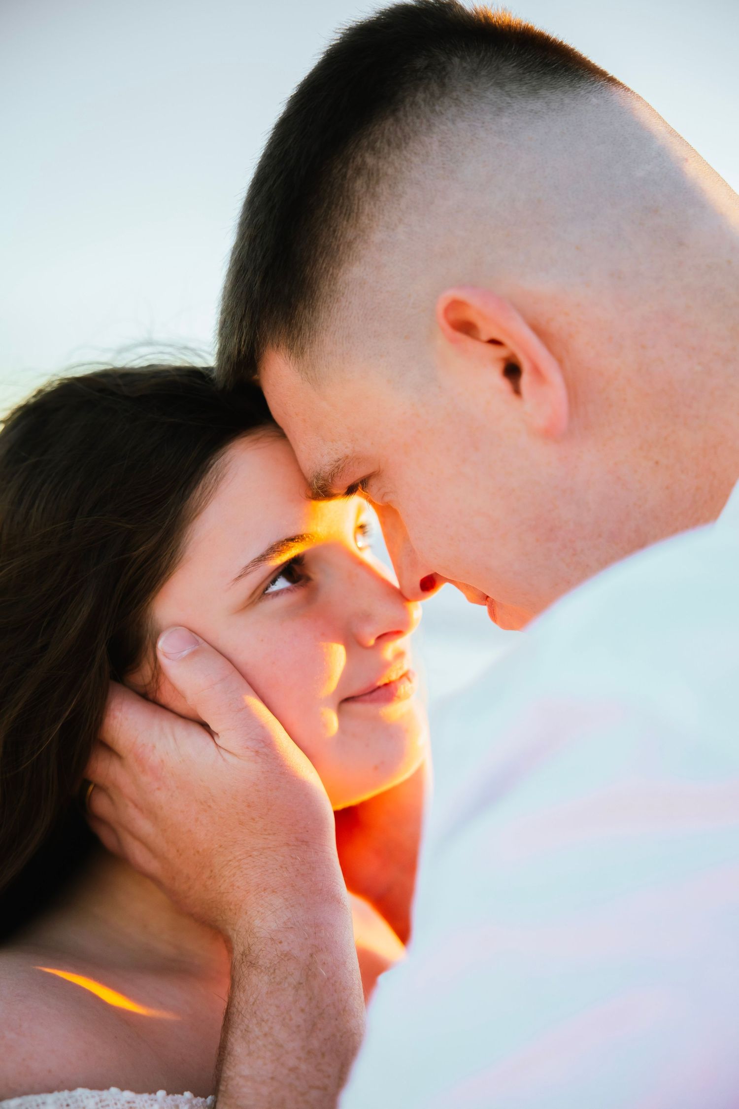 Romantic couple sharing tender moment at sunset, man gently cupping woman's face as they gaze at each other.