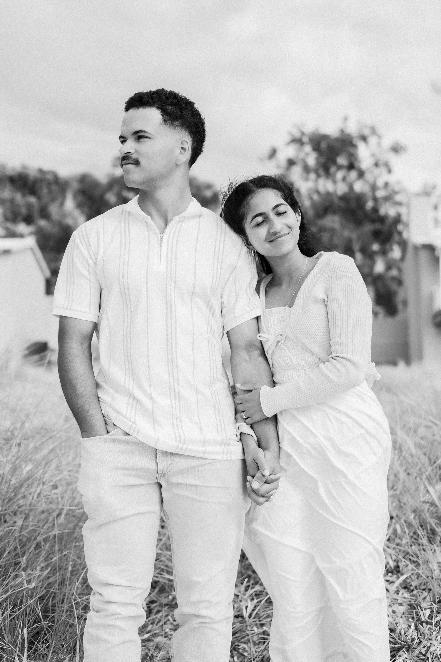 Black and white photo of couple standing together, woman resting head on mans shoulder peacefully.