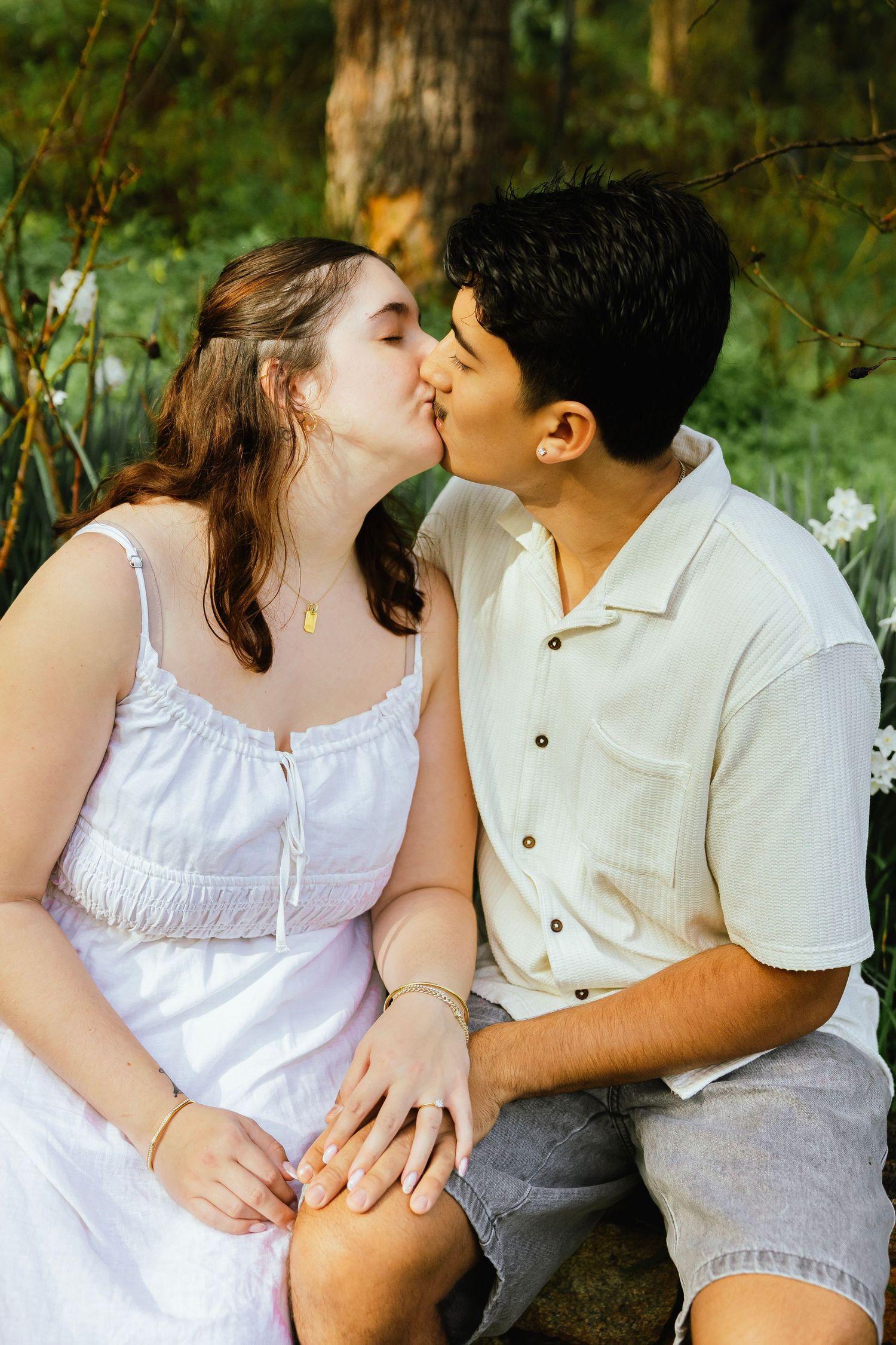 Young couple sharing a romantic kiss while sitting together in a lush green garden setting.