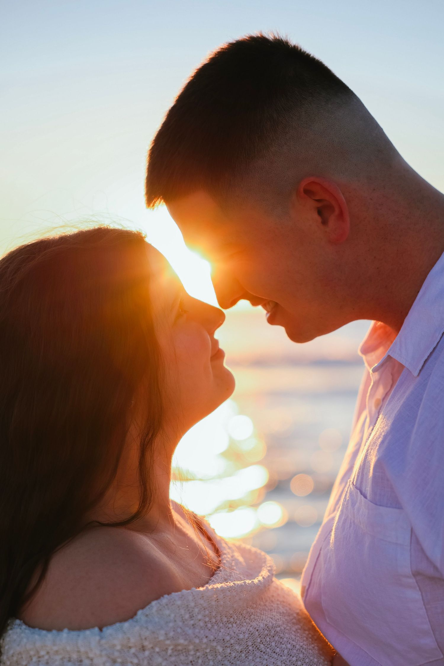Romantic couple sharing an intimate moment at sunset by the ocean, with golden light glowing between them.