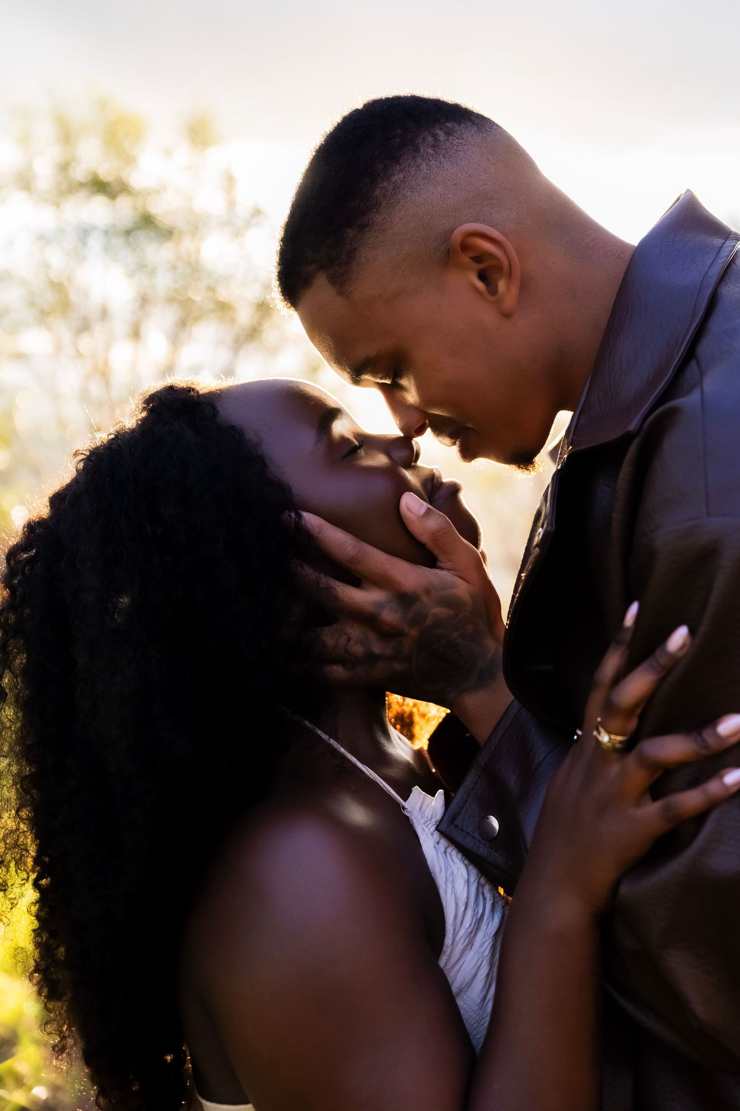 A romantic couple sharing an intimate moment, foreheads touching, bathed in warm golden sunset light outdoors.