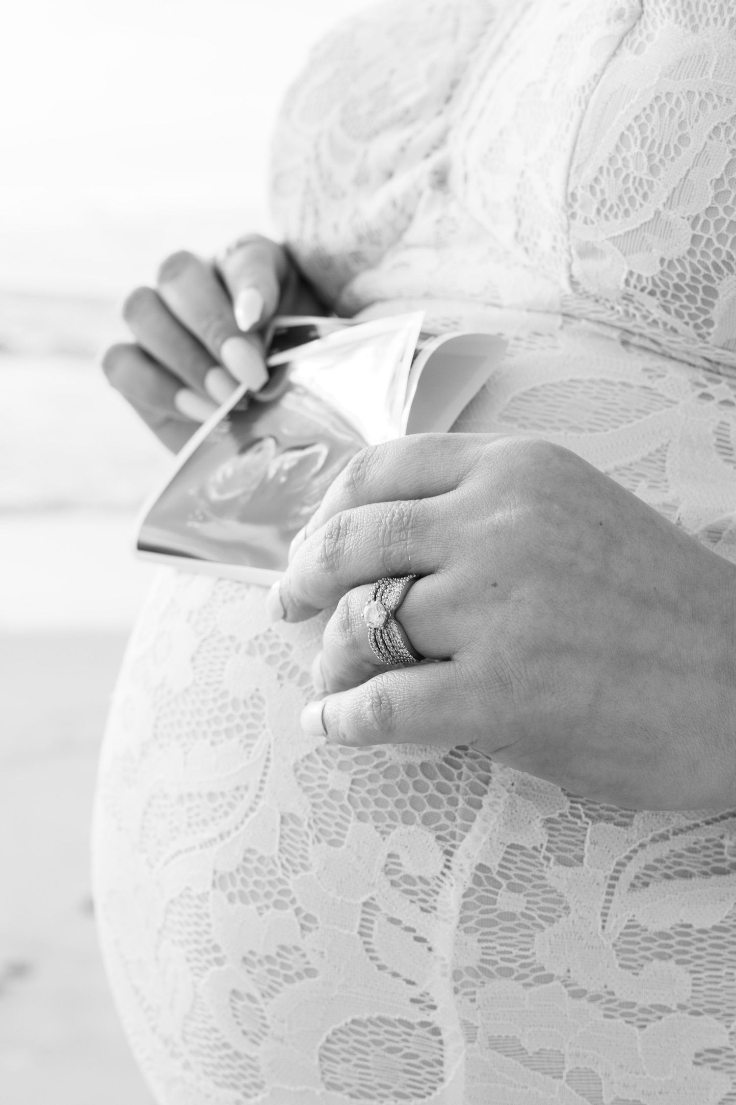 Black and white close-up of pregnant woman holding ultrasound photos in lace dress.
