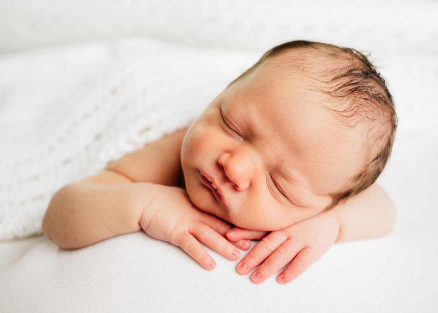 Sleeping newborn baby resting on folded hands on a soft white blanket