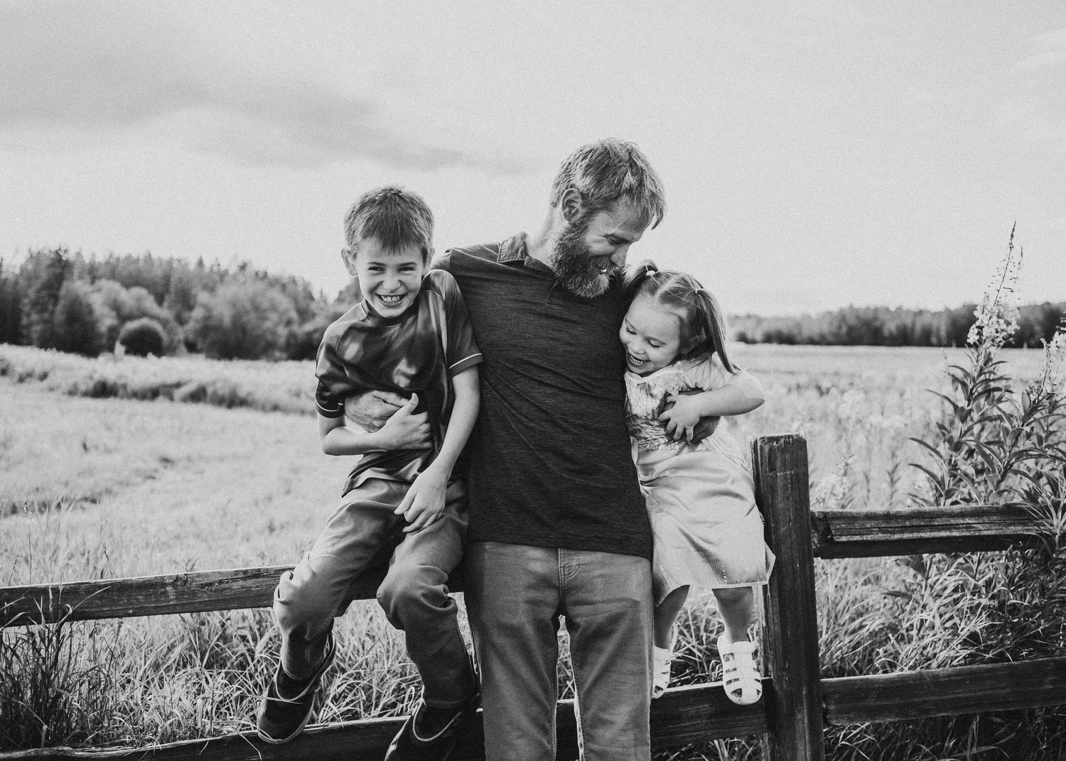 Parent standing between two children sitting on a wooden fence during an outdoor family photography session
