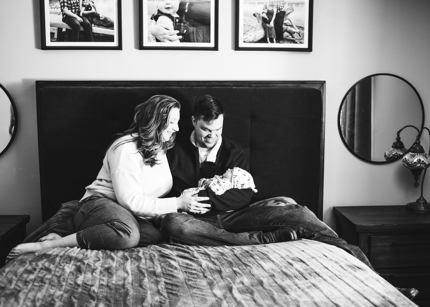 Parents cuddling their newborn baby together on a bed during an in-home newborn session