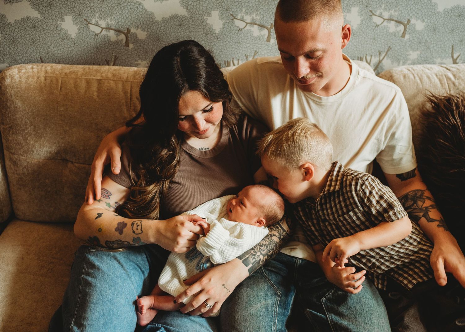Parents cuddling their newborn baby with their young child on a couch during a family session