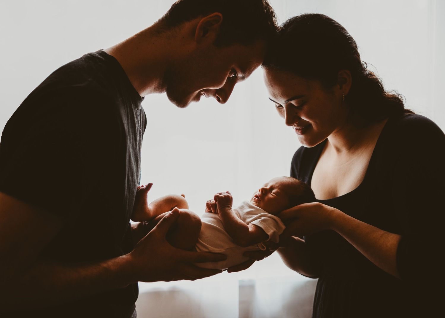 Parents gently holding their newborn baby together during an in-home newborn photography session