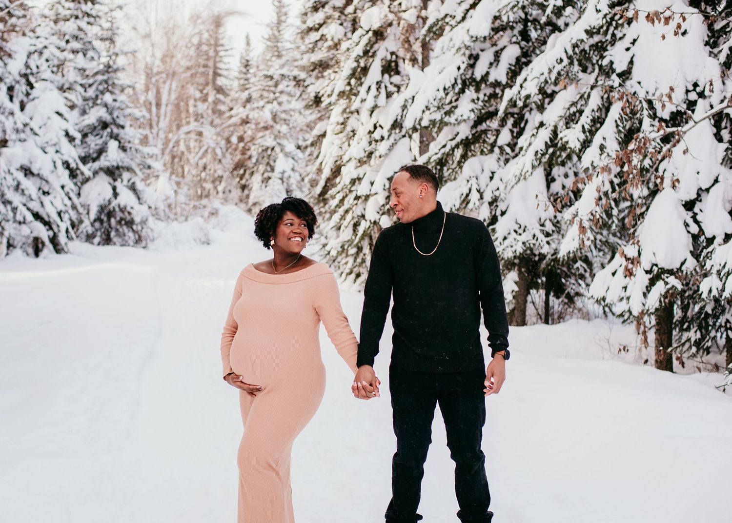 Expecting couple walking hand in hand through a snowy winter forest during a maternity session