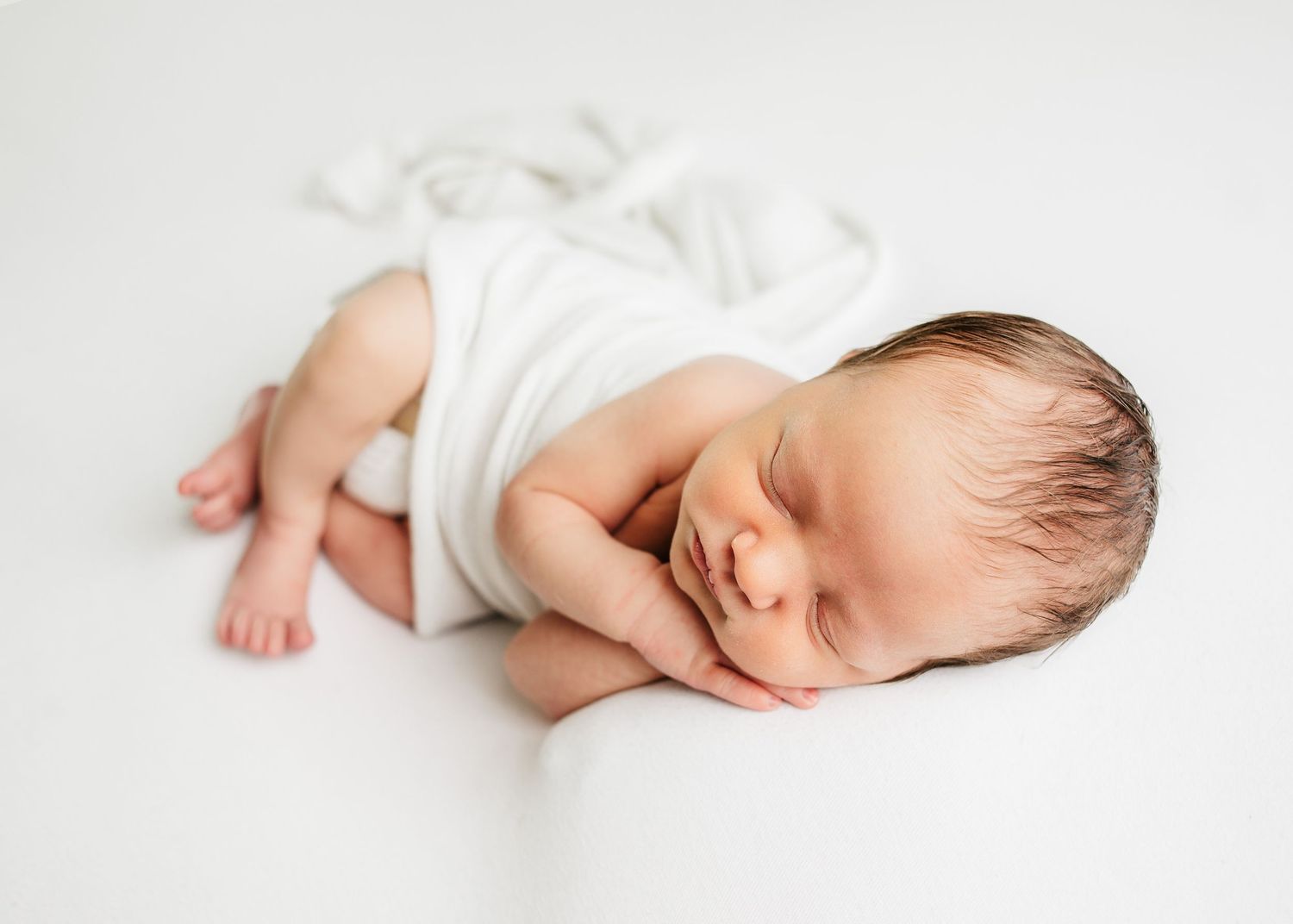 Sleeping newborn baby lying on a white blanket with hands tucked beneath their head
