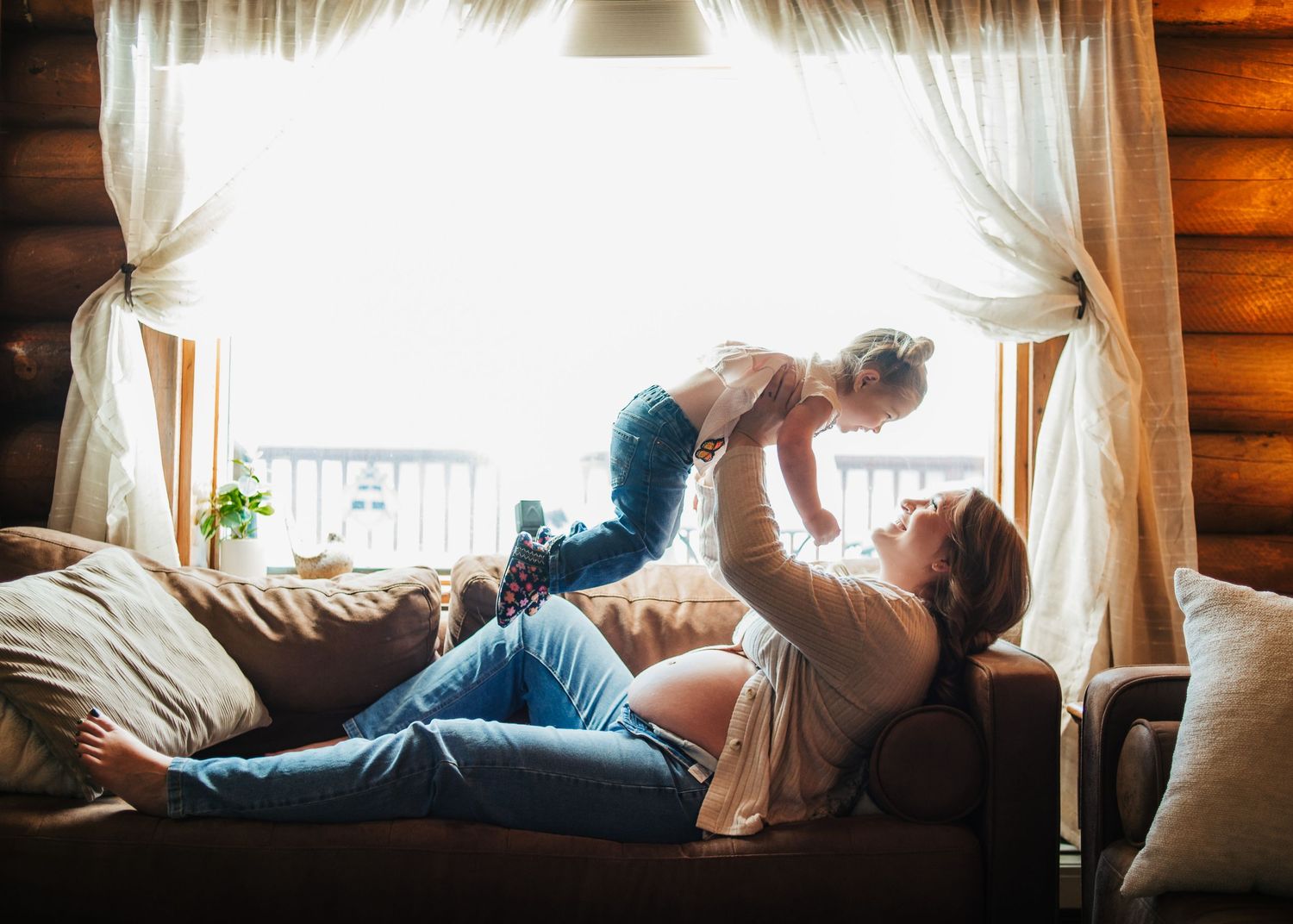 Expecting mother and child playing together on a couch at home during a maternity session