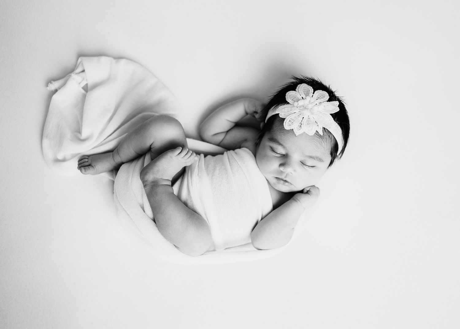 Sleeping newborn baby wrapped in a white blanket and wearing a floral headband