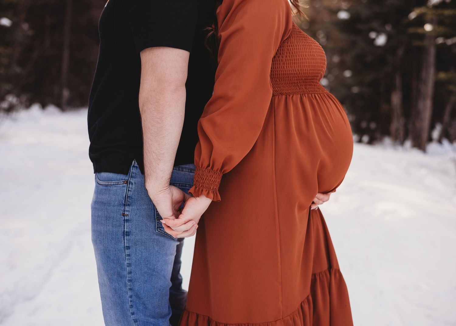 Expecting couple holding hands outdoors in a snowy winter setting during a maternity session