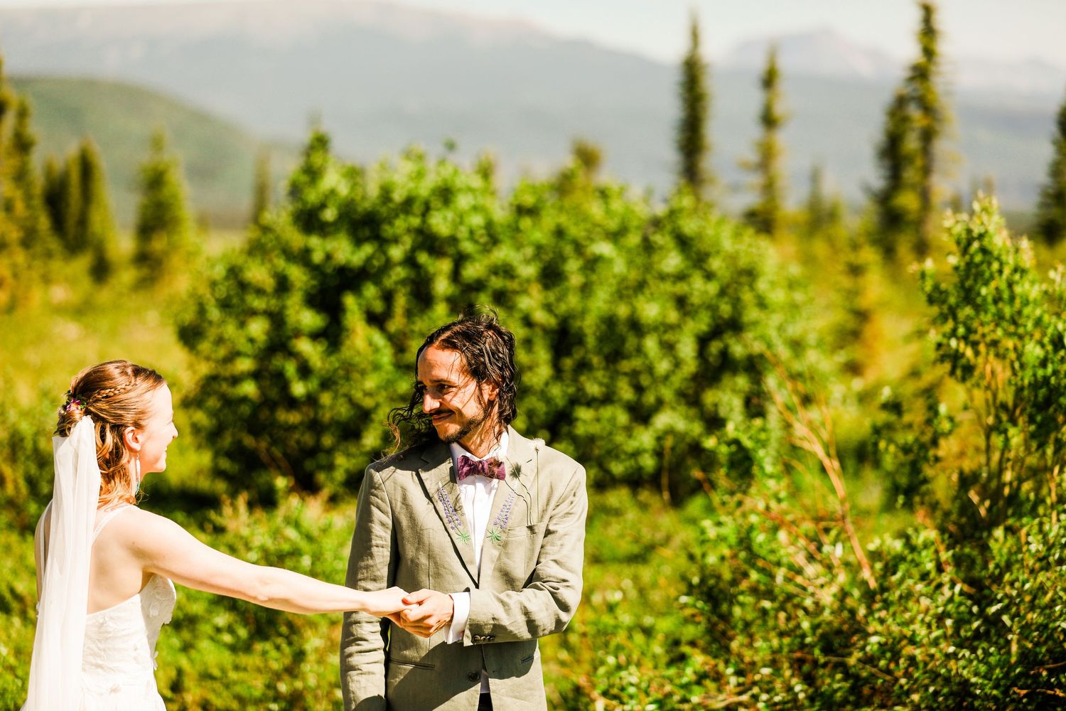Couple dances together in sunlit mountain meadow surrounded by evergreen trees.
