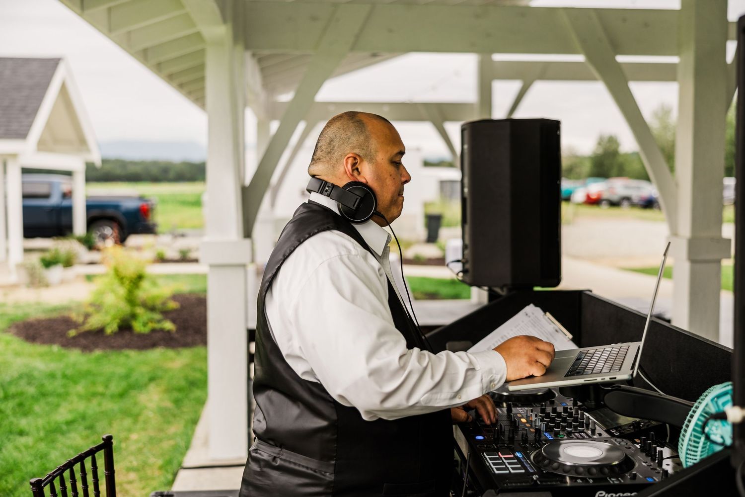 DJ works at laptop computer station under covered outdoor venue during wedding event.