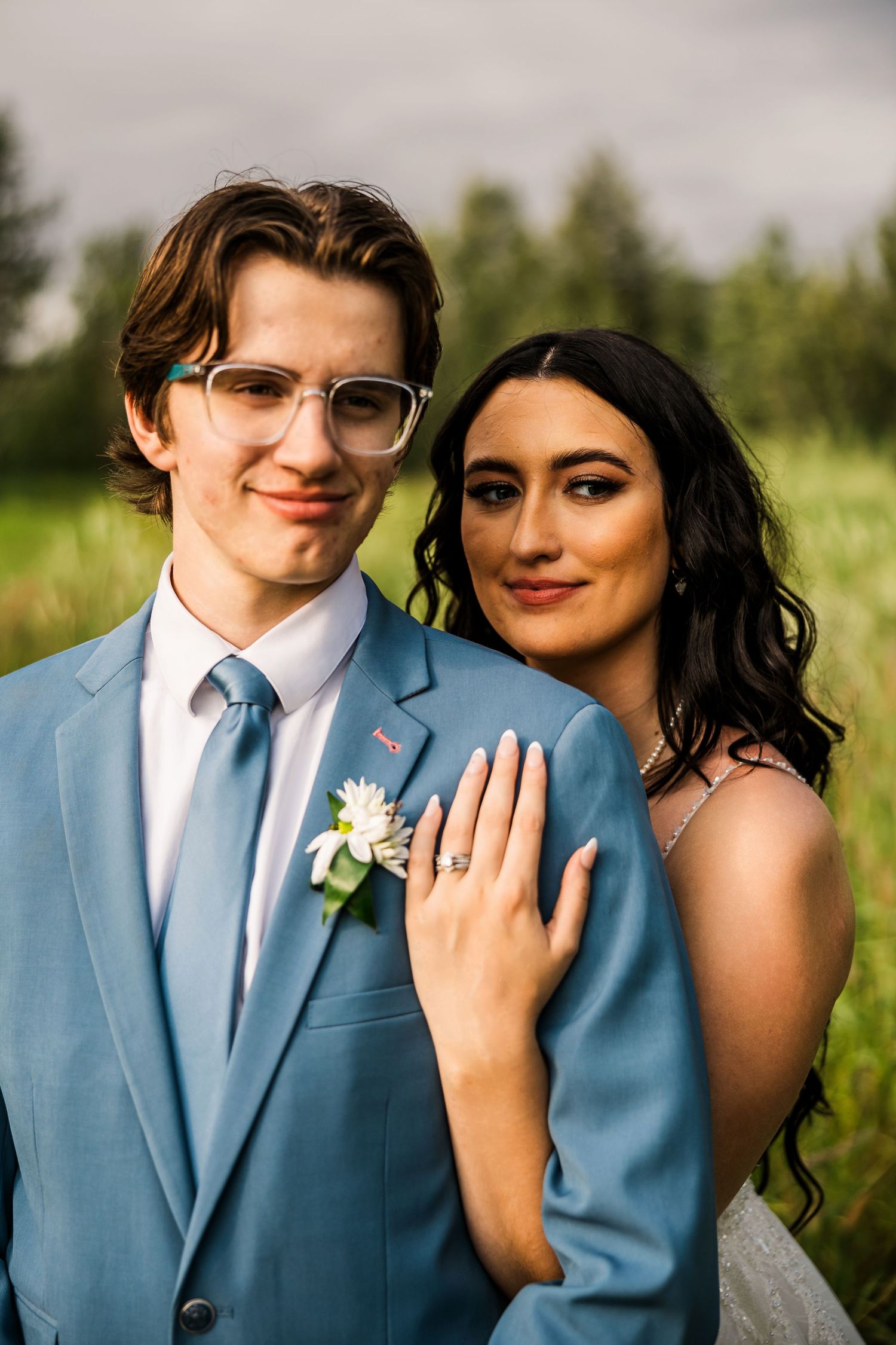 A formal couple poses together outdoors with natural greenery in the background.