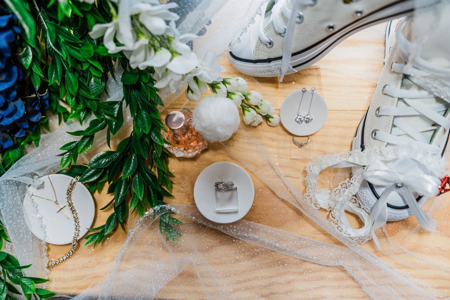White sneakers and wedding decor items arranged on a wooden surface with greenery accents.